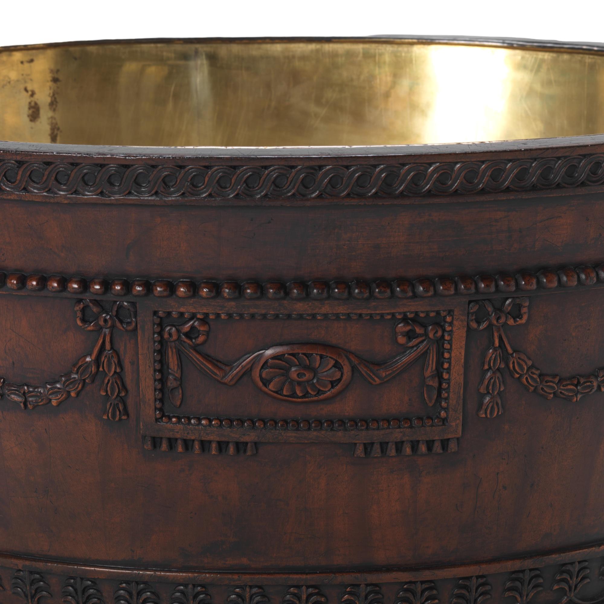 A George III design ormolu mounted mahogany oval wine cooler after a design by Robert Adam, attributed to Sefferin Nelson, circa 1772-4. The rim with carved and gilded entrelac border, the body with carved ribbon-tied trailing husk garlands centred