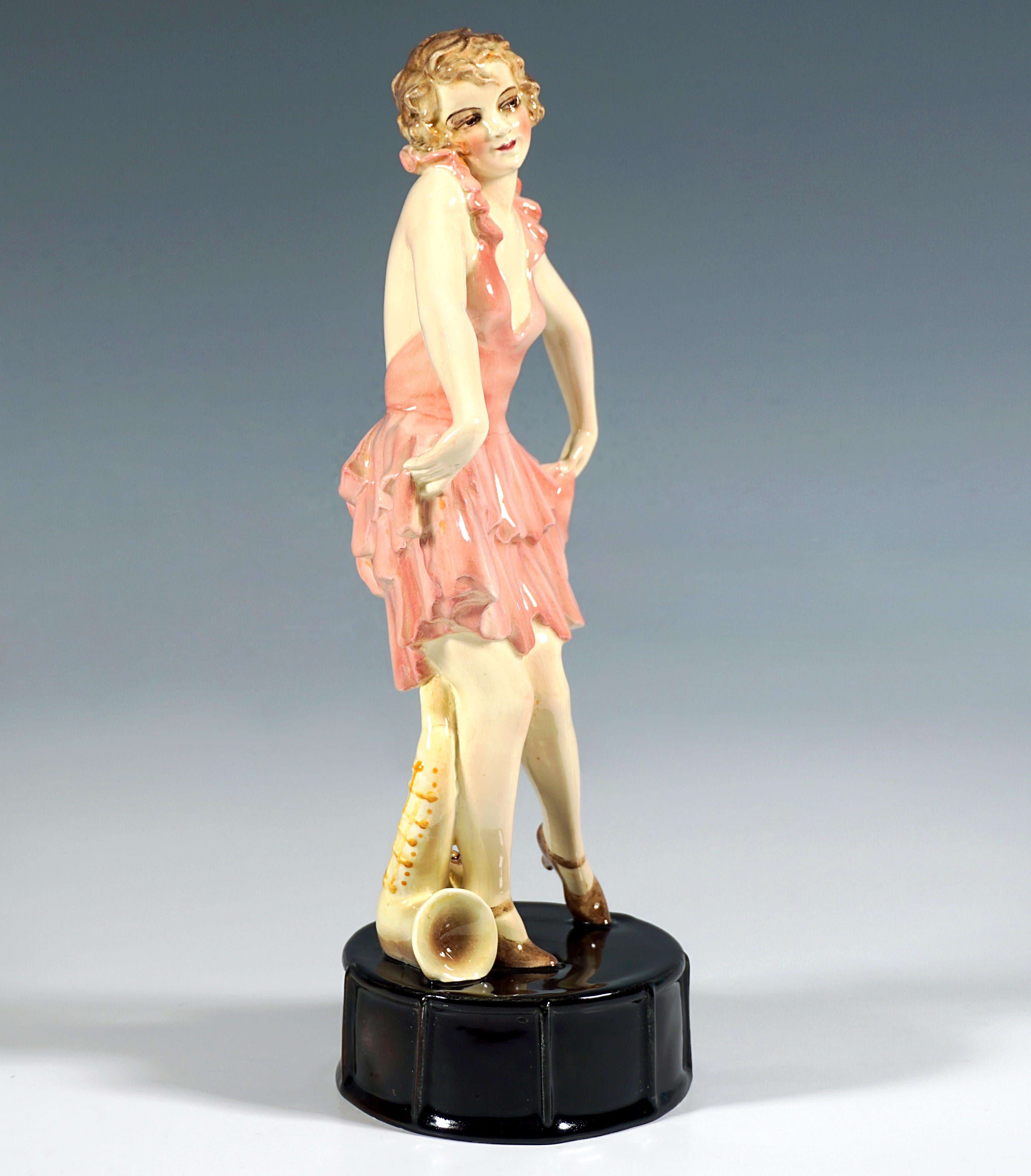 Rare Goldscheider Art Déco ceramic figure of the 1920's:
Depiction of a young vaudeville dancer posing in a short, low-cut, backless, light pink dress with ruffled flounces and a bow, holding up the hem of her skirt to both sides and curtsying.
The