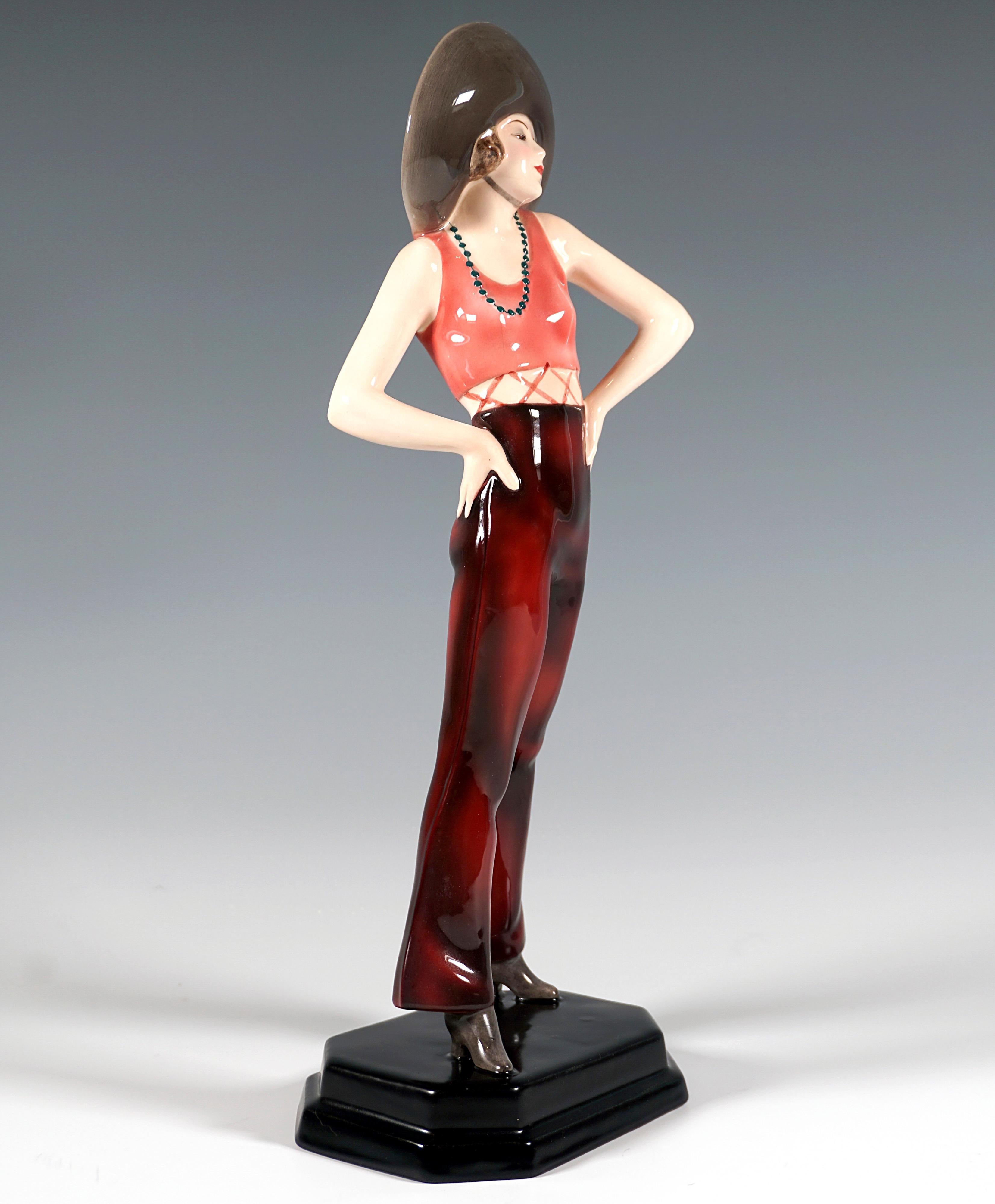 Sehr seltene Kunstkeramikfigur um 1929:
Mädchen mit breitkrempigem Hut auf den kurzen Locken, ärmelloses, kurzes Oberteil, mit langer Schlaghose und Cowboystiefeln an den Füßen, steht breitbeinig und hat die Hände in die Hüften gestemmt, um den Hals