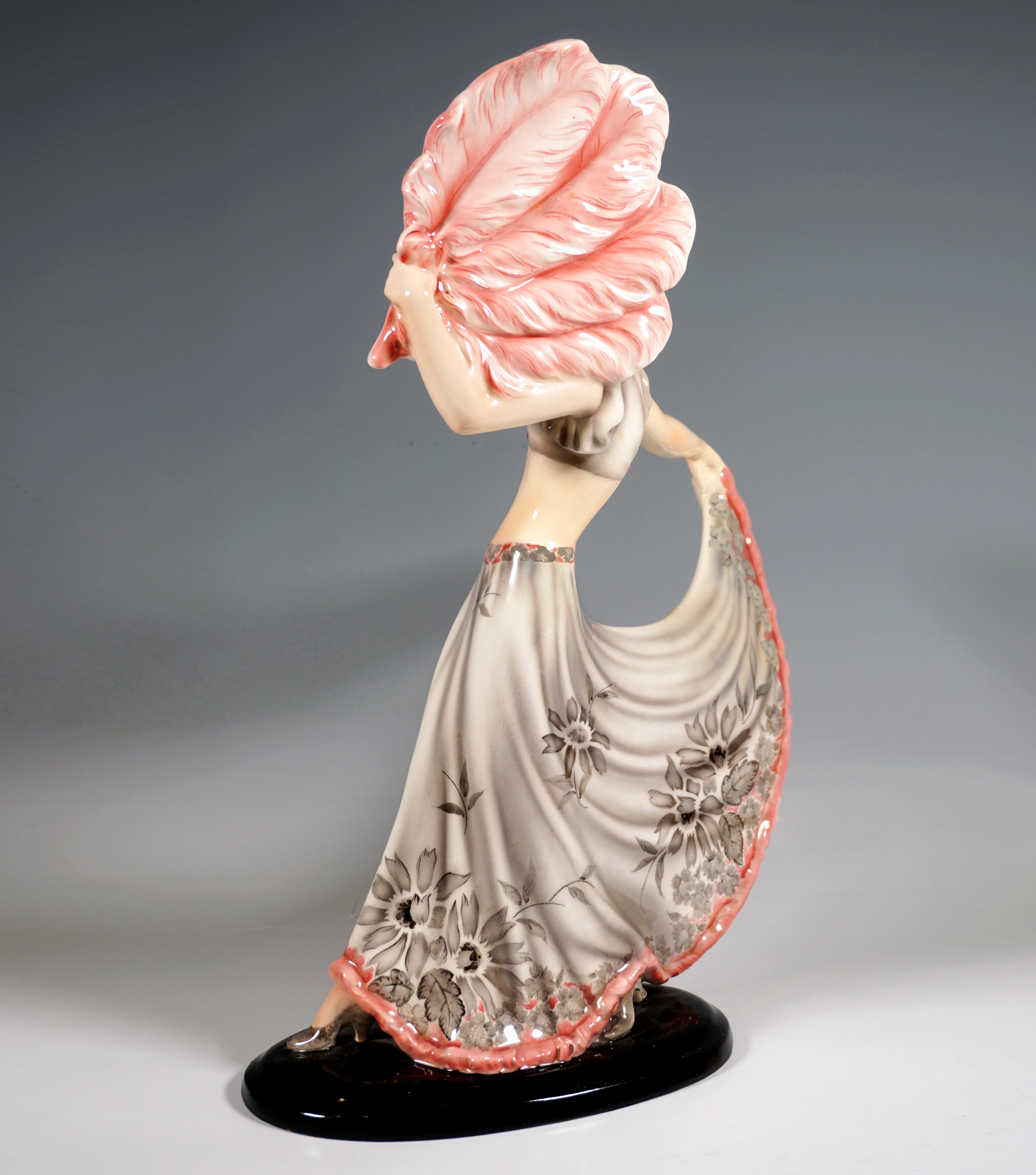 Elegante Goldscheider Art Deco Keramikfigur aus den 1930er Jahren: 
Tänzerin mit schulterlangem Haar in einem langen, weiten, grauen Rock mit Blumendekoration und rosafarbenem Saum und passendem Bustier, nach rechts blickend, das rechte Bein nach