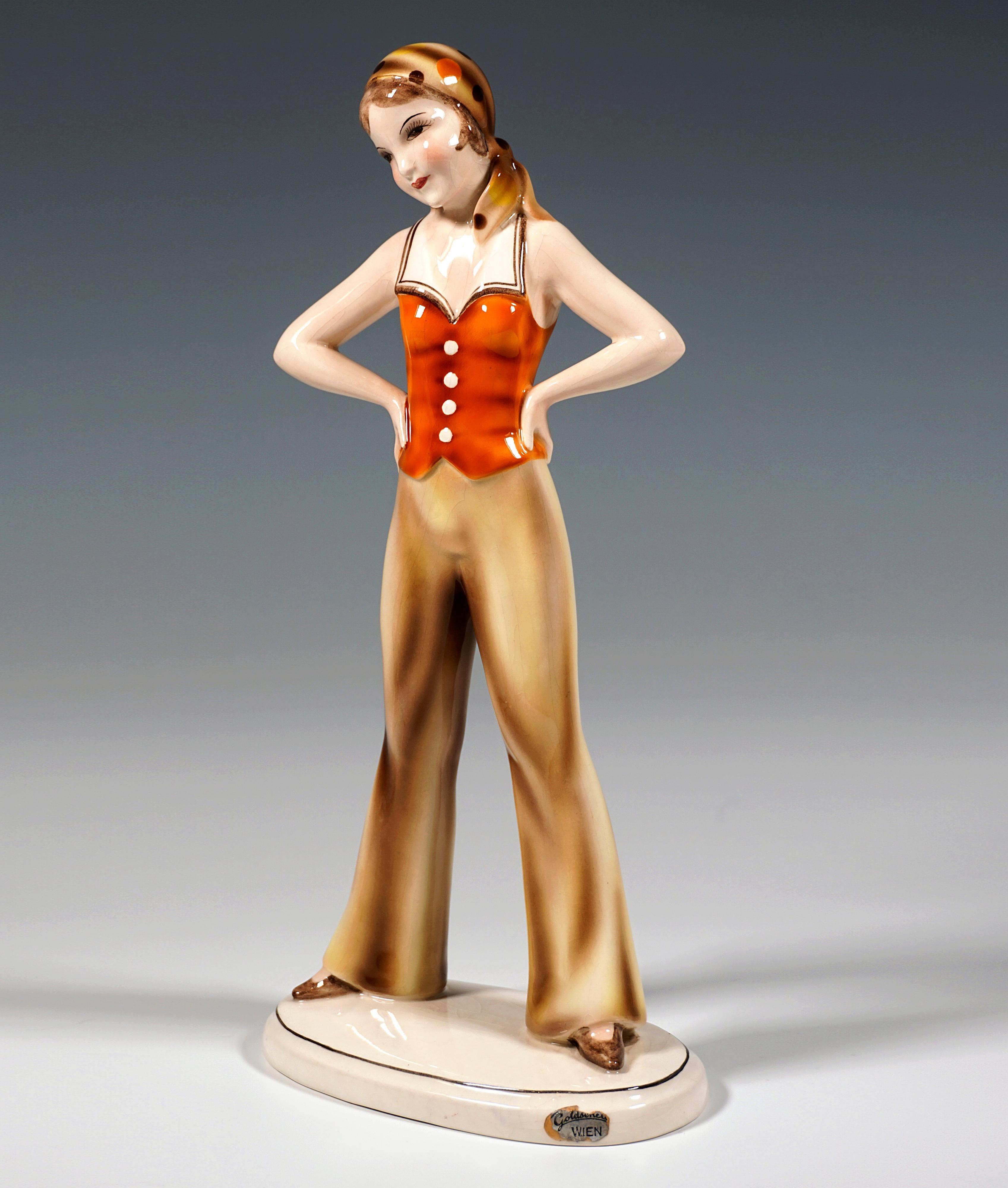 Very rare art ceramic figurine of the 1930s:
Standing girl with a dotted headscarf tied to the back of her head in orange and brown tones, dressed in a sleeveless orange top with a white collar and buttons at the front, long beige flared pants and