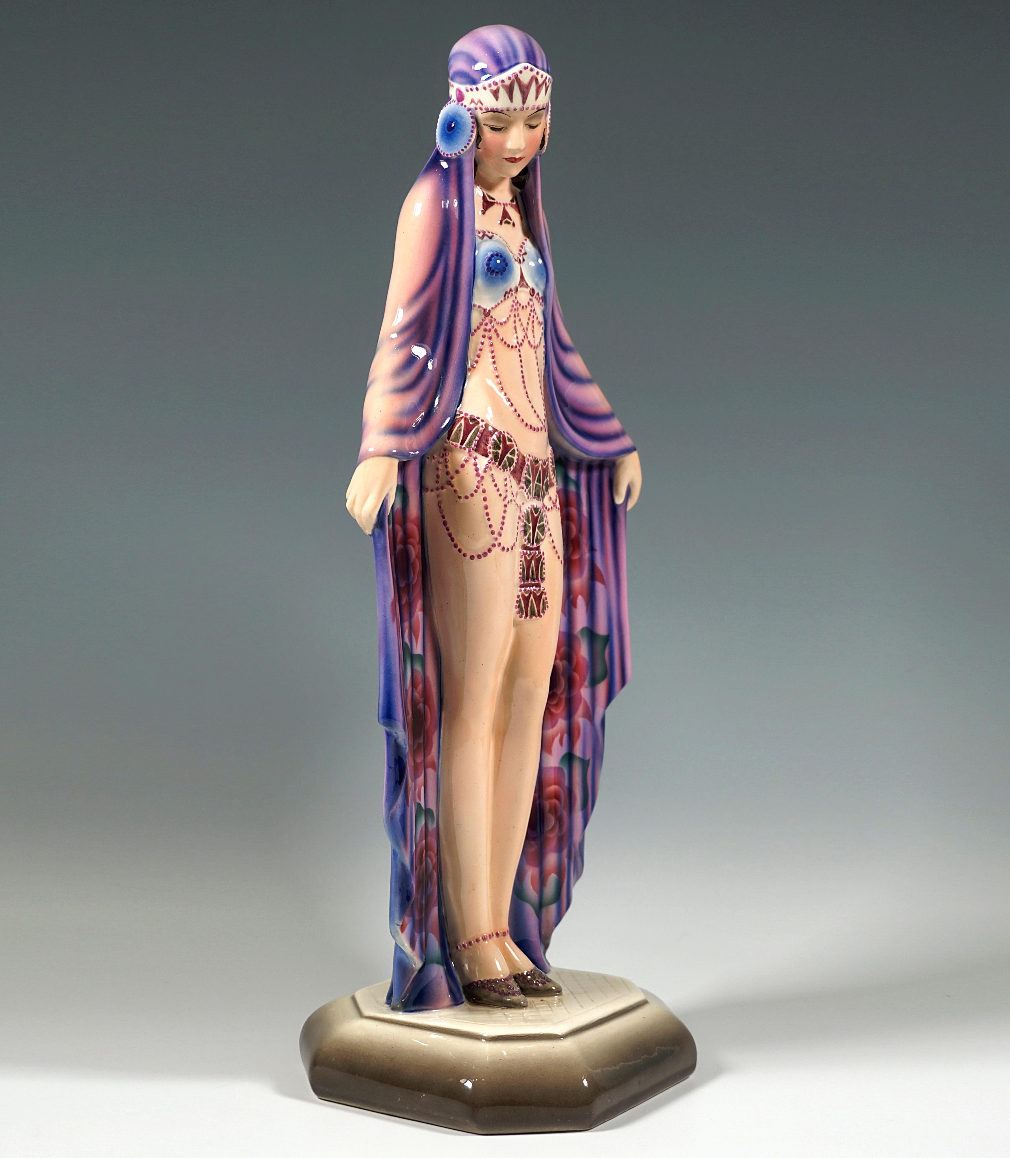 Very rare and exceptional Goldscheider Art Deco ceramic figurine:
Depiction of a standing young lady with lowered head in oriental garb, wrapped in a large violet-coloured cloth reaching down to the floor, the front of which is decorated with
