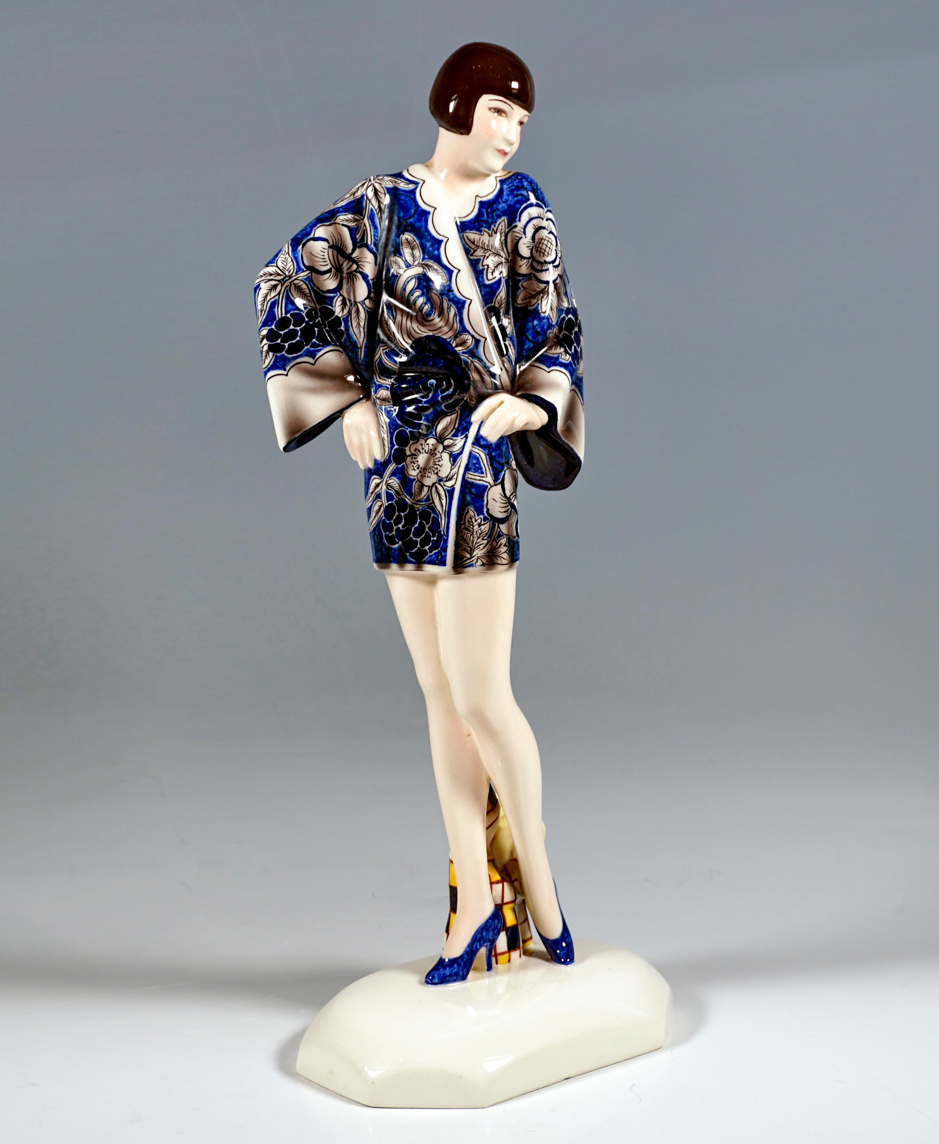 Excellent art ceramic figurine from the 1930s:
Young lady with bob hairstyle standing upright, torso turned to the left and supporting both arms on the hips, in a short blue kimono with a floral pattern and high heels. Behind her between the legs