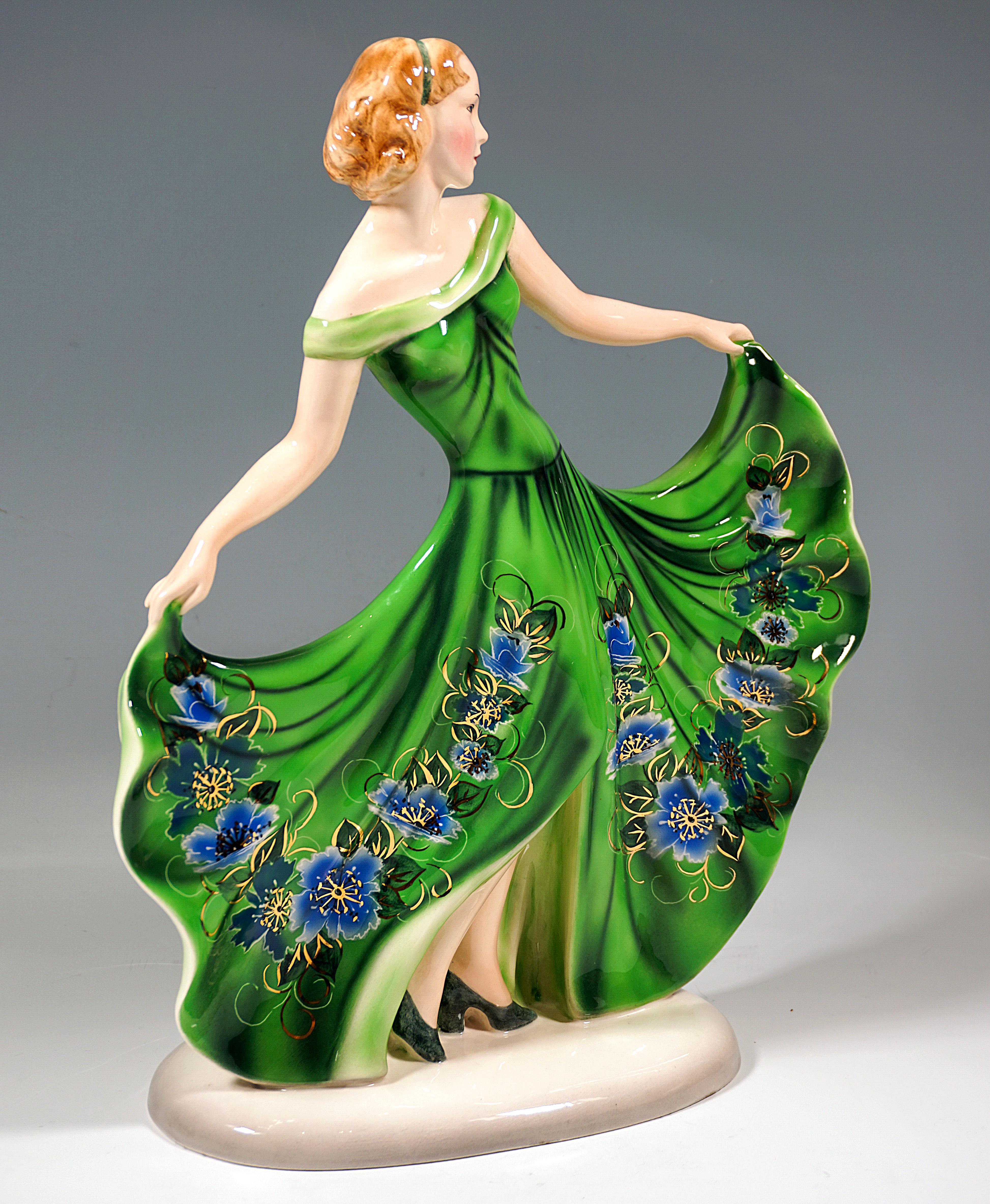 Very rare Goldscheider Vienna ceramic figure of the 1930s:
Young pretty lady, chin-length hair fastened with a hair band, posing in a long green dress with a wide, high-slit skirt decorated with flowers, which she holds up with both arms stretched