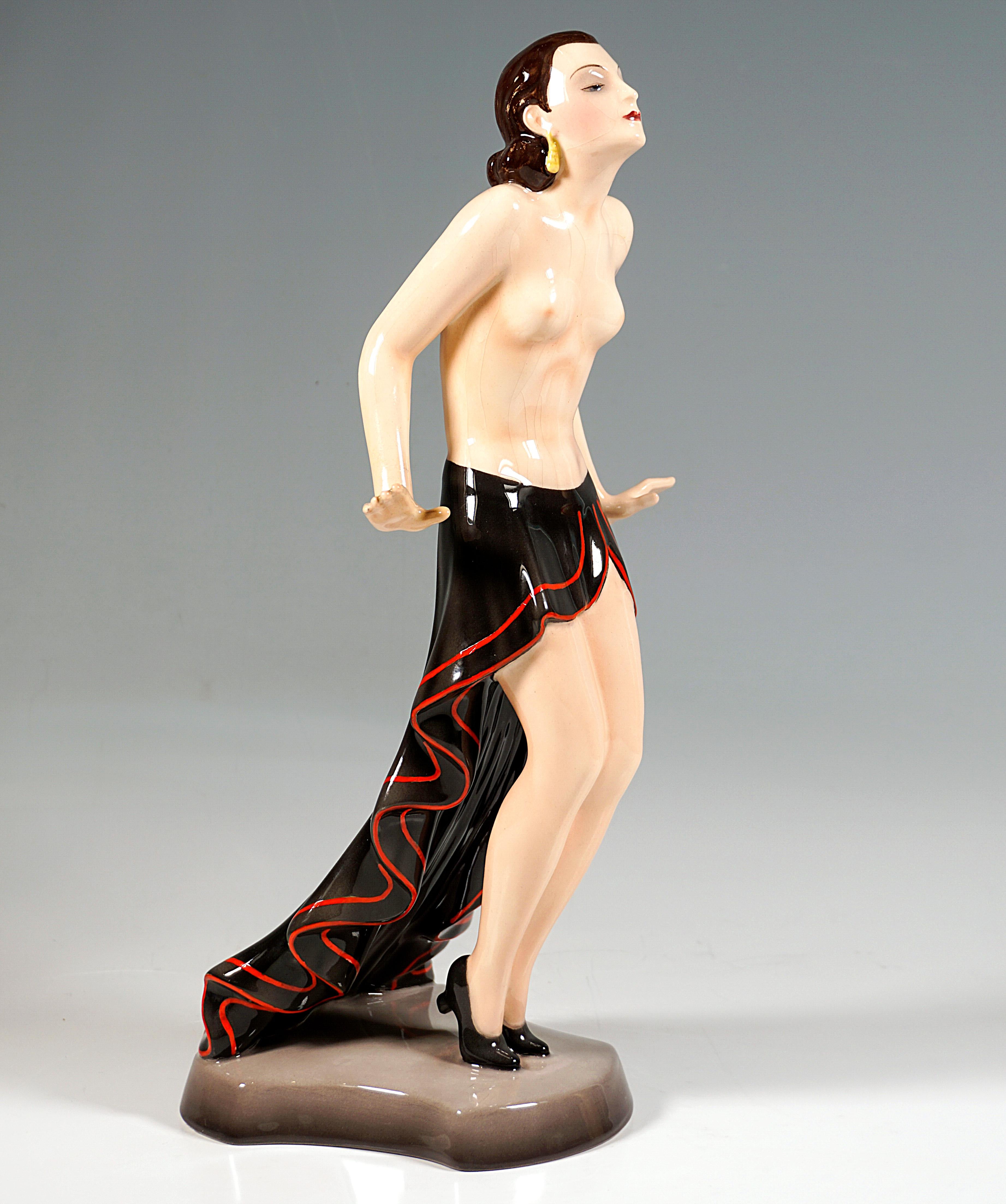 Very Rare Goldscheider Ceramic Figurine of the late 1930s:
Standing young, pretty revue dancer with dark hair tied together at the nape of the neck and earrings, posing with a bare upper body and a black short flounced skirt with a long train and