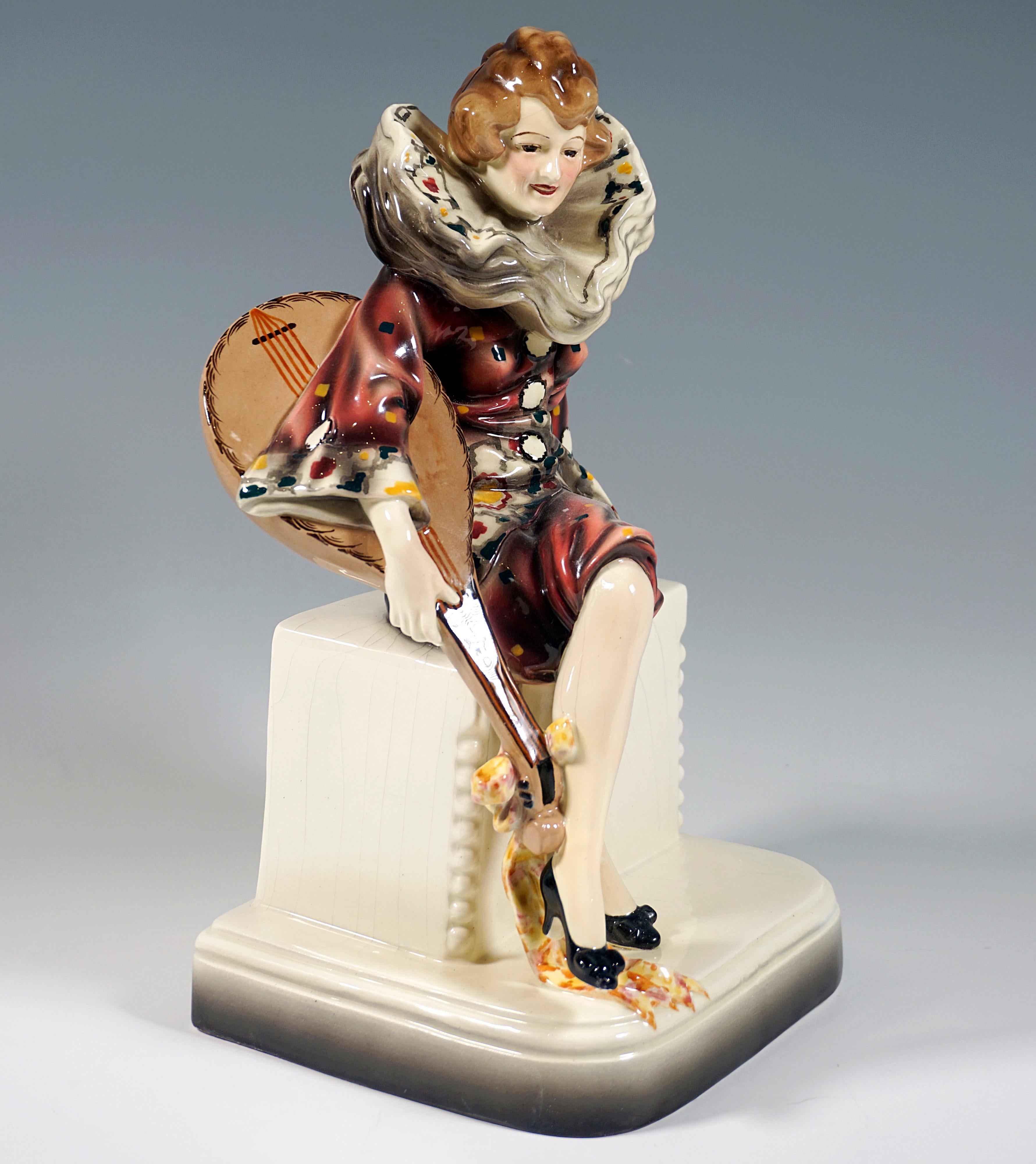 Rare Art Ceramic Figure of the 1920s:
Depiction of a young musician dressed as Pierrette, sitting on a pedestal with her lute, wearing a wide red costume with knee-length harem pants and particularly large beige ruff, the garments decorated with