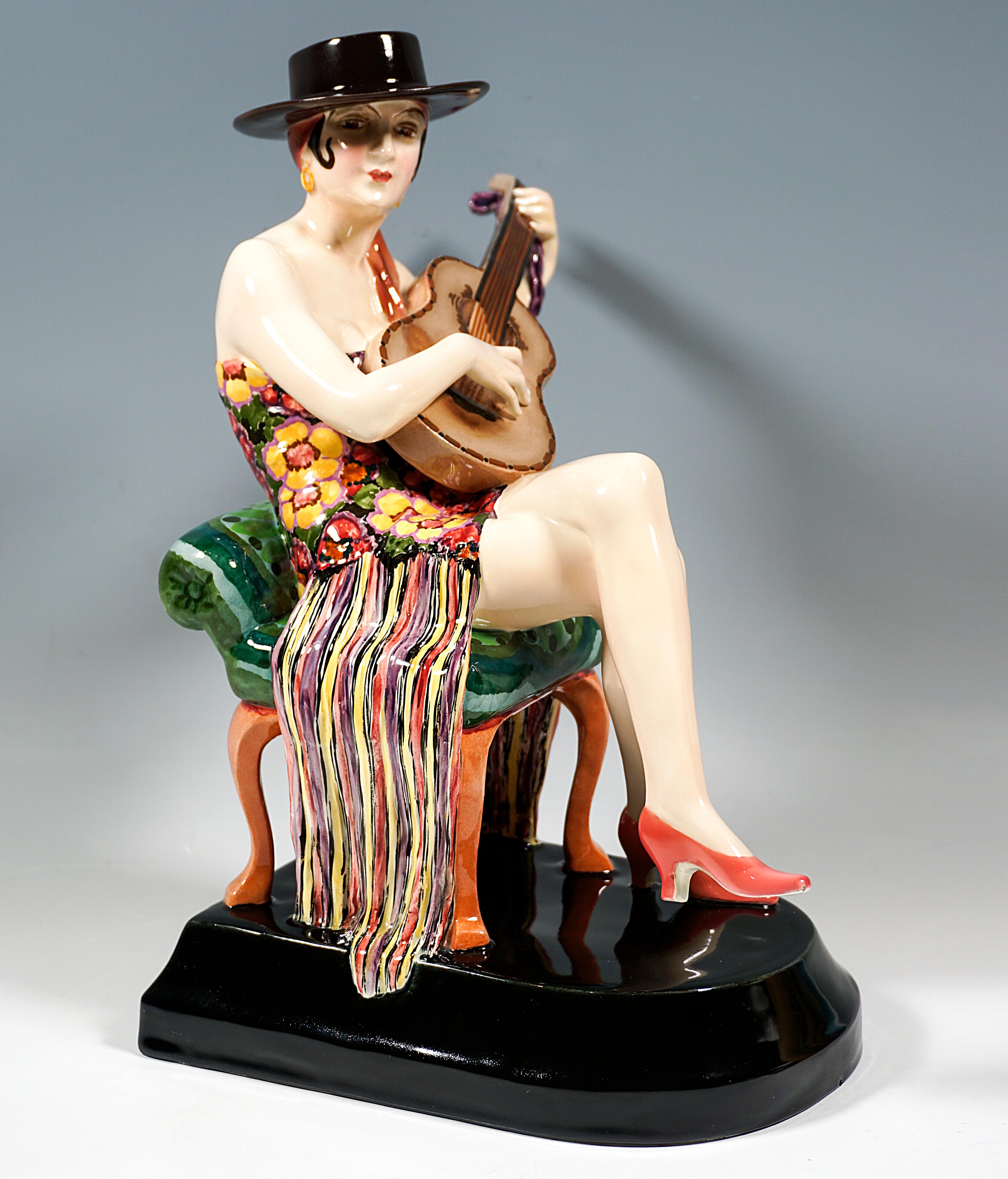 Excellent and Rare Goldscheider Vienna Art Déco Ceramic Figurine: 
Dancer sitting on a small bench upholstered with green fabric, wearing a short, strapless costume with colorful floral decoration, her legs crossed, playing a guitar, wearing a