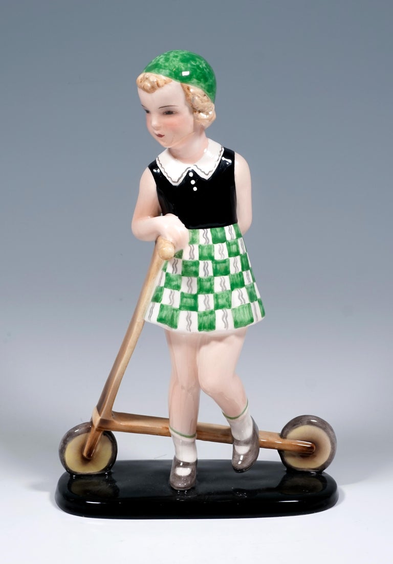 Very rare Goldscheider Vienna figurine of the 1930s.
Girl with a green cap, black sleeveless blouse with white collar, green and white checked skirt, white socks and light brown shoes leaning on a wooden scooter.
On a black, elongated flat base