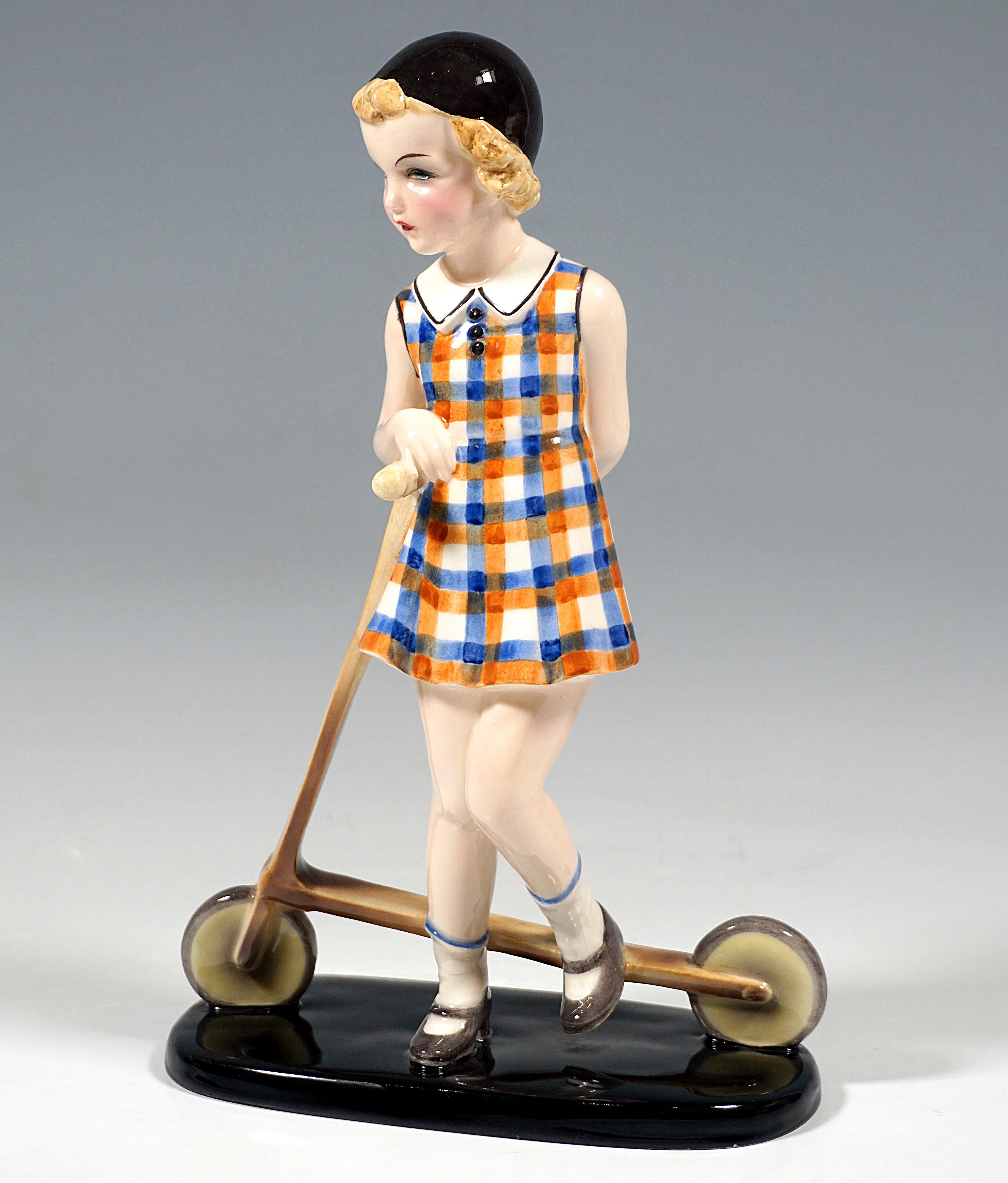 Rare Goldscheider Vienna Figurine of the 1930s.
Girl with a black cap, in a blue, orange and white checkered dress with a white collar, white stockings and brown shoes, leaning on a wooden scooter.
On a black, elongated flat base with rounded