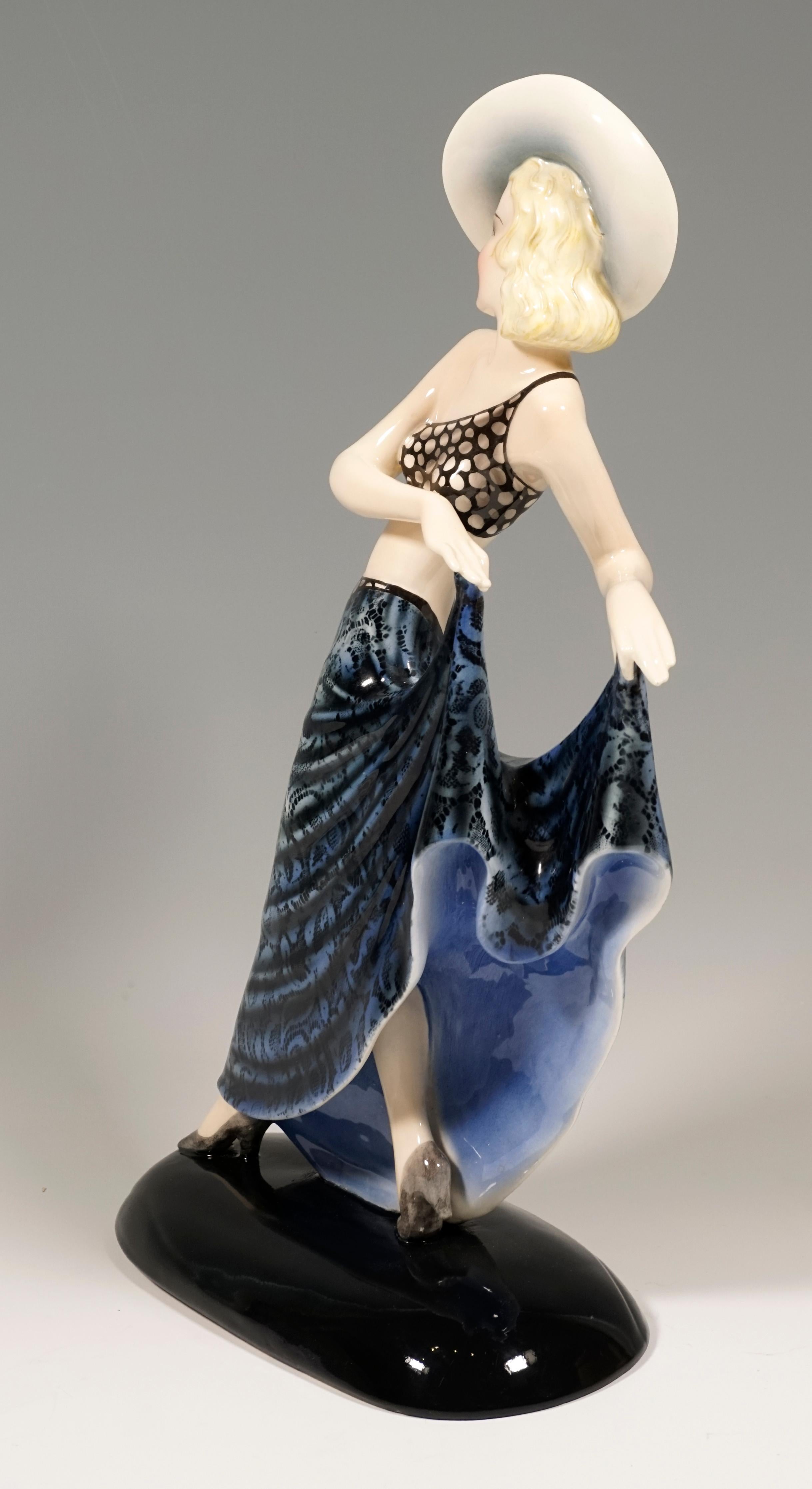 Rare Viennese ceramic art from the 1930s:
Striding young lady with a large hat, holding up the long, wide skirt with blue lace pattern with both hands.
On a black oval base.

Based on the film 'The Blonde Dream', starring Lilian