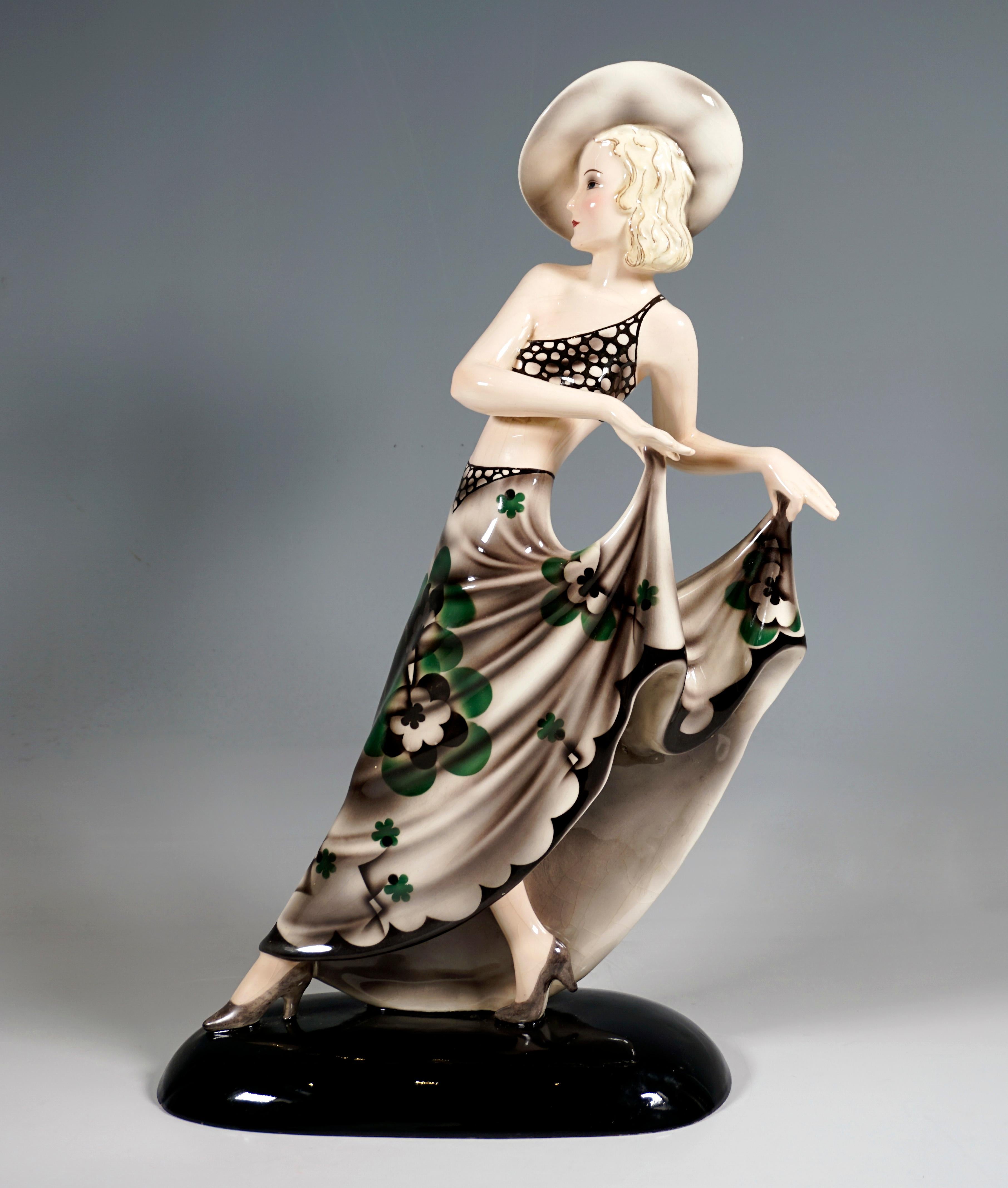 Excellent art ceramic figurine from the 1930s:
Striding young lady with a cropped, delicate top and a large hat, holding up the long, wide skirt with a stylized floral pattern with both hands.
On a black oval base, artist's signature 'Dakon' on