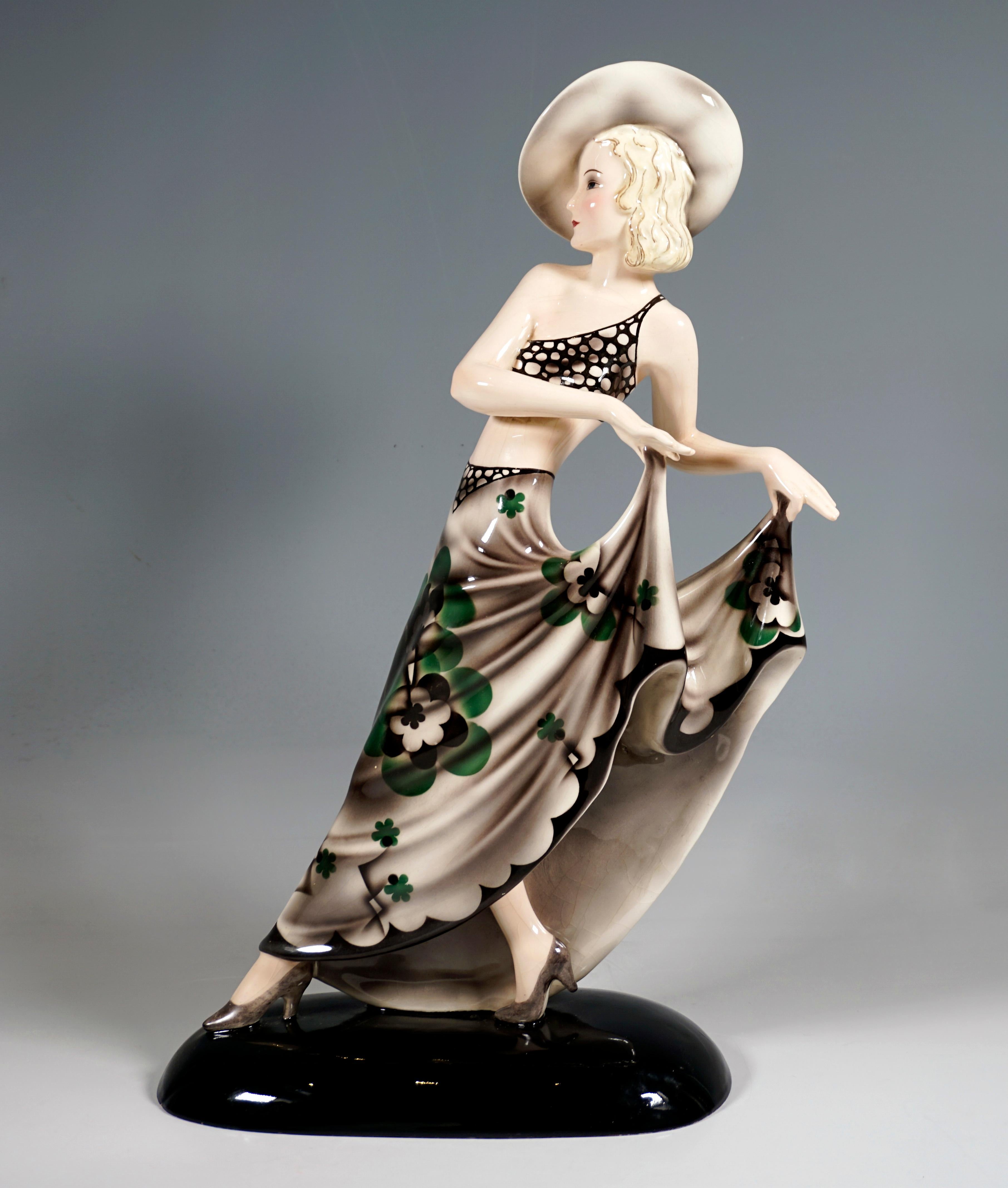 Excelente figurita de cerámica artística de los años 30:
Jovencita a grandes zancadas con un delicado top recortado y un gran sombrero, sosteniendo con ambas manos la larga y amplia falda con un estilizado estampado floral.
Sobre una base oval