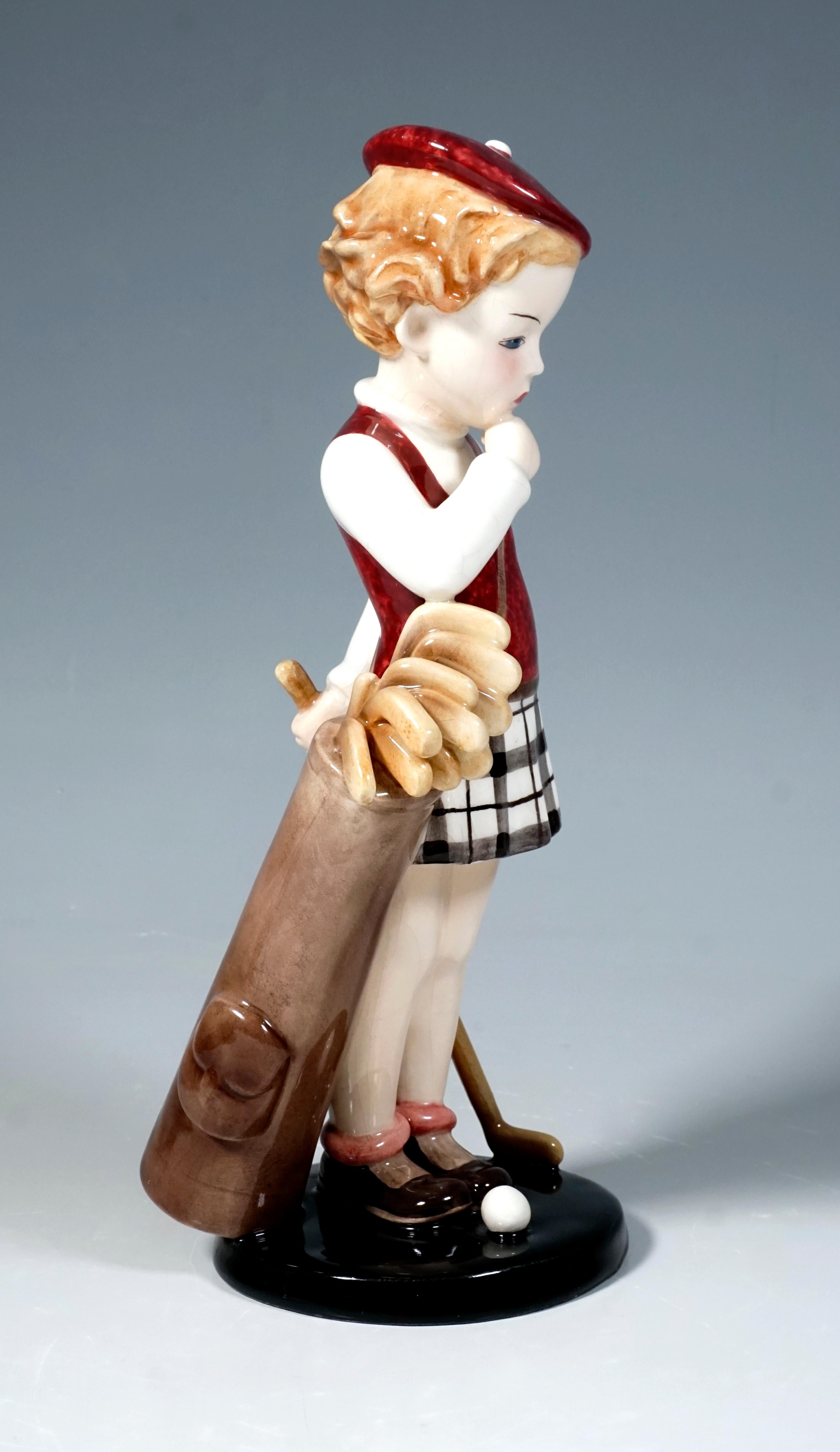 Goldscheider Vienna figurine of the 1930s.
Standing girl in golf clothes: camisole with red pollunder, checked skirt and red beret, carrying a golf bag with clubs and holding a club behind her.
On a black, round base.

Designed by Stephan Dakon