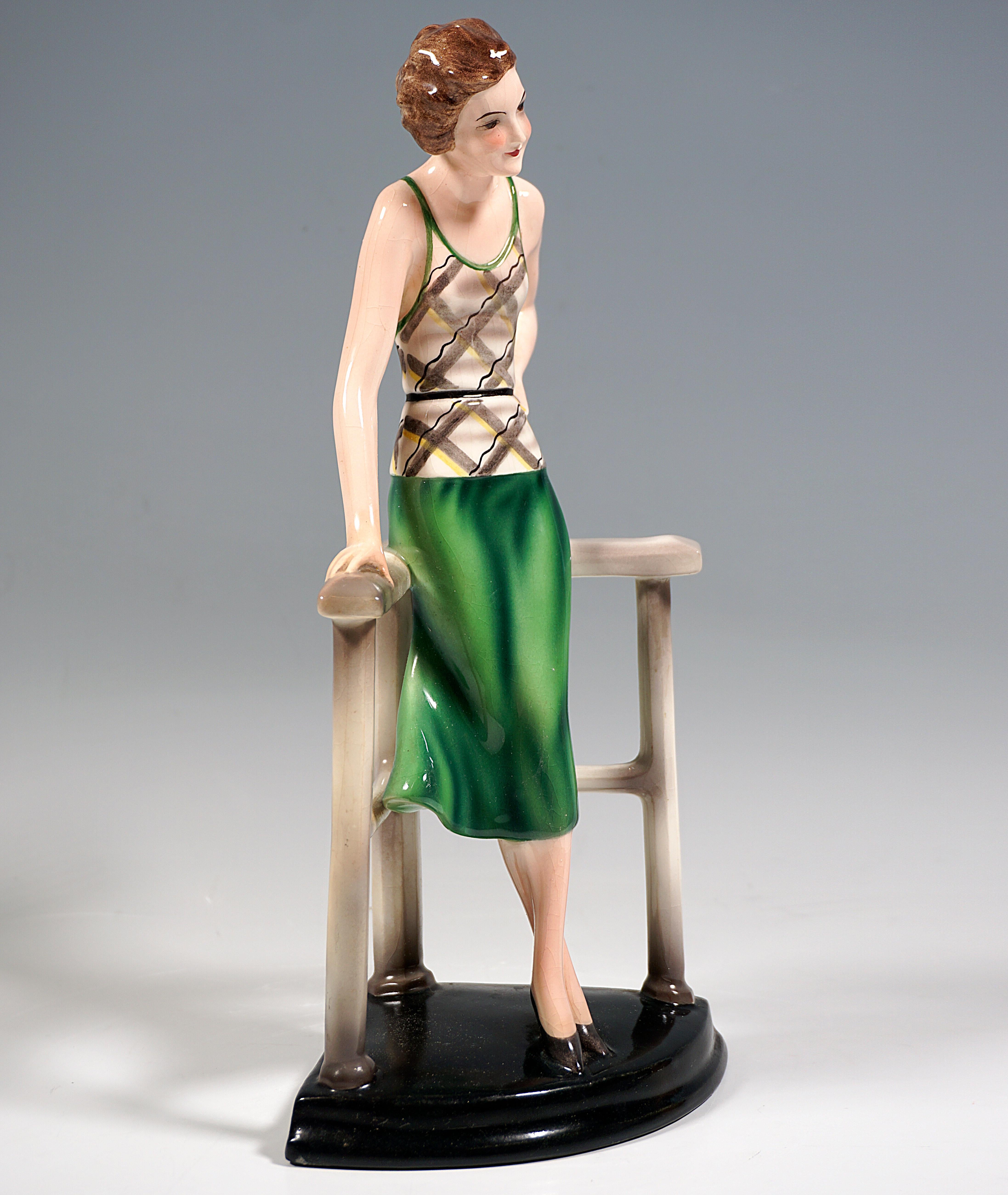 Very Rare Goldscheider Vienna Ceramic Figurine of the 1930s:
Standing young lady with brunette, chin-length curly hair in beige and gray plaid low-back top with green straps and green skirt, legs crossed and left hand on hip, leaning casually