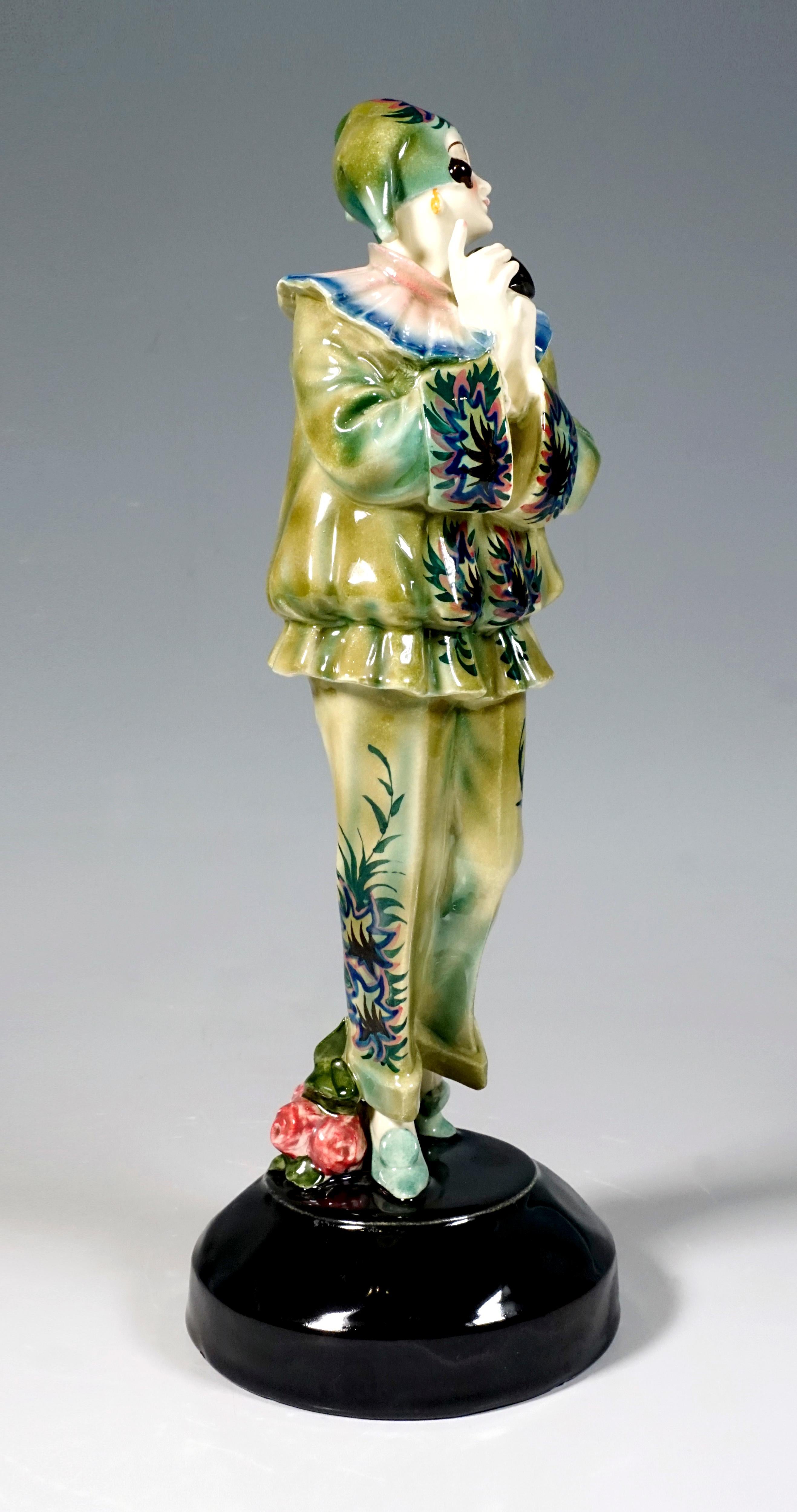 Finest Viennese ceramic art from the 1920s:
The standing young lady holds a black mask in front of her in her folded hands and looks dreamily to the side. She wears a green two-piece suit with a slouchy top and ruff and a three-pronged cap. The