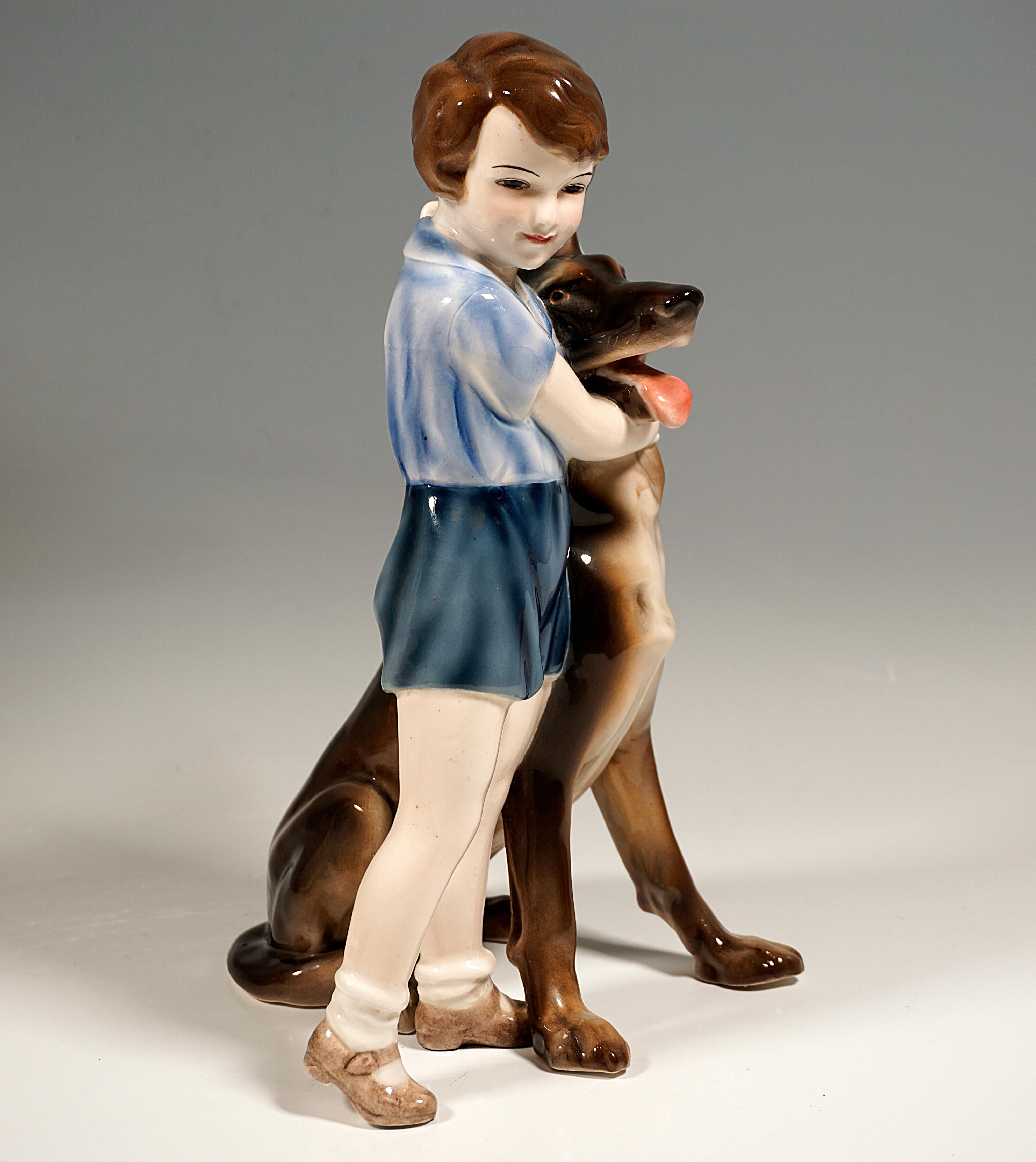 Standing girl with brunette hair, in a short-sleeved light blue blouse and short blue trousers, shoes with stockings, standing next to and embracing a seated German Shepherd.
Without base.

The artist Josef Lorenzl is responsible for the standing