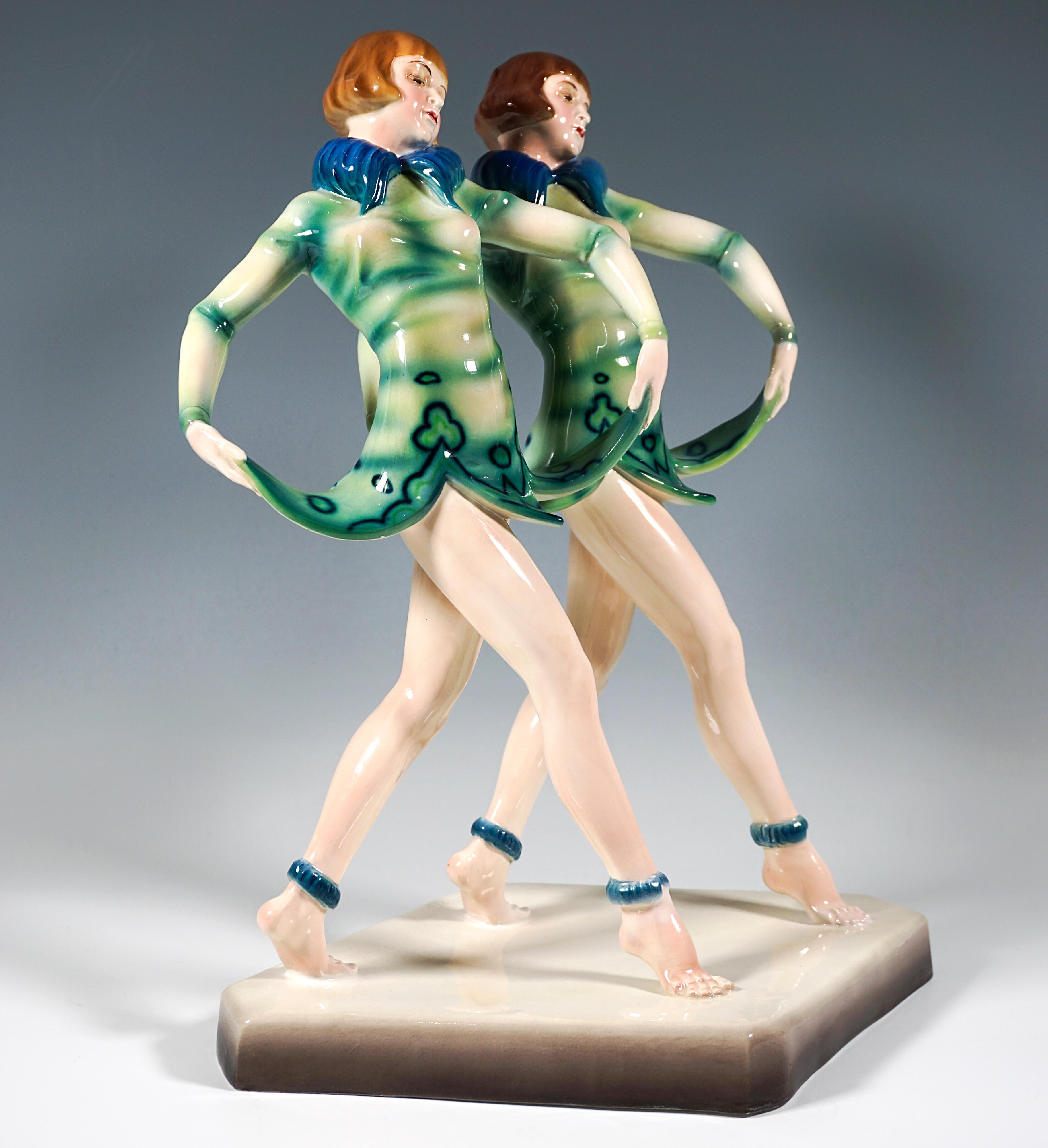 Bemerkenswerte und seltene Goldscheider Art-Déco-Figurengruppe aus den späten 1920er Jahren:
Zwei posierende junge Revue-Zwillinge mit Pagenfrisuren, die parallel einen Schritt vorwärts machen und dabei mit beiden Händen den glockenblumenförmigen