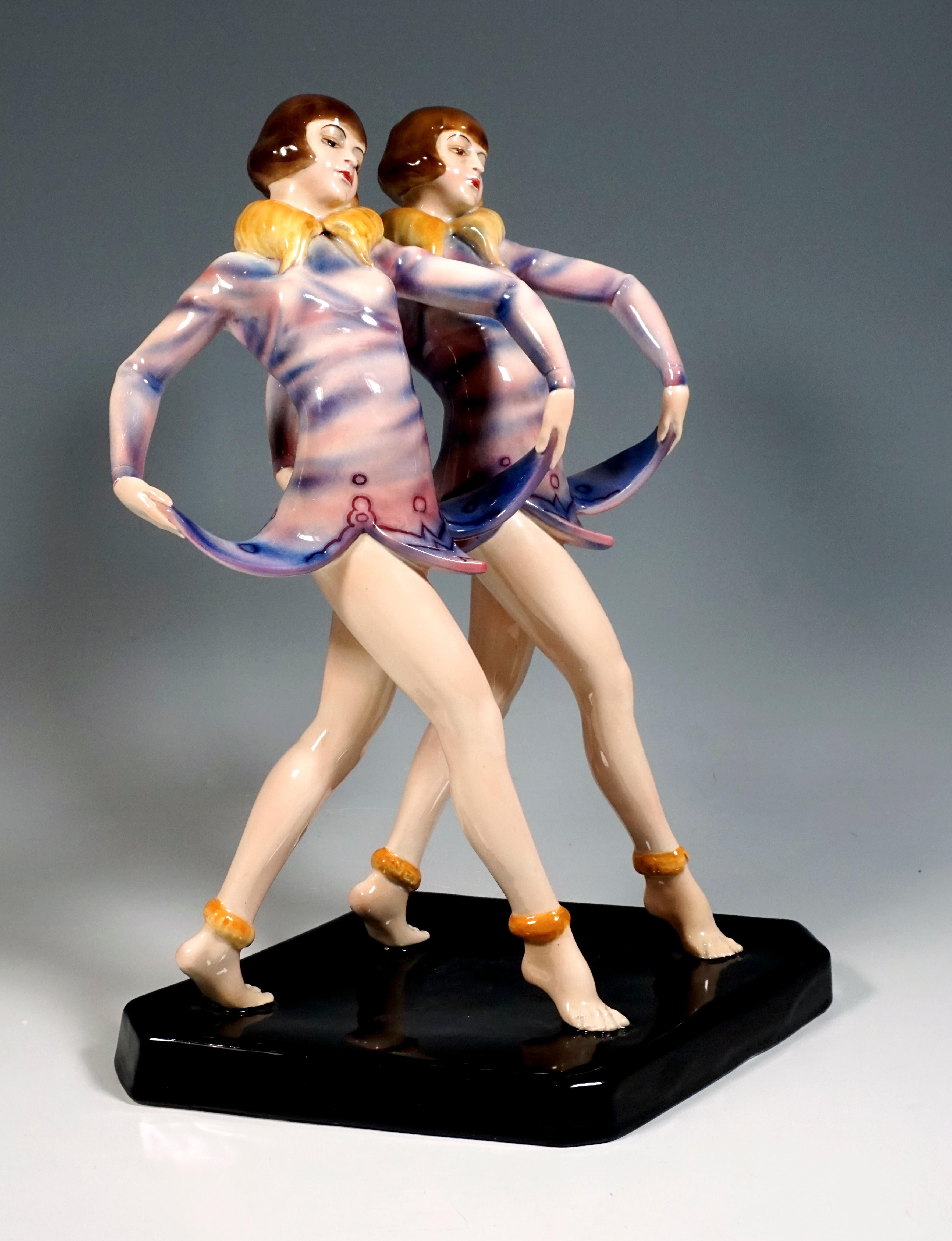 Most Remarkable Rarest Goldscheider Art Deco Figurine Group of the 1930s:
Two standing young revue twin dancers with pageboy hairstyle, taking a step forward. At the same time, they lift the bellflower-shaped hem of their short purple dress with a