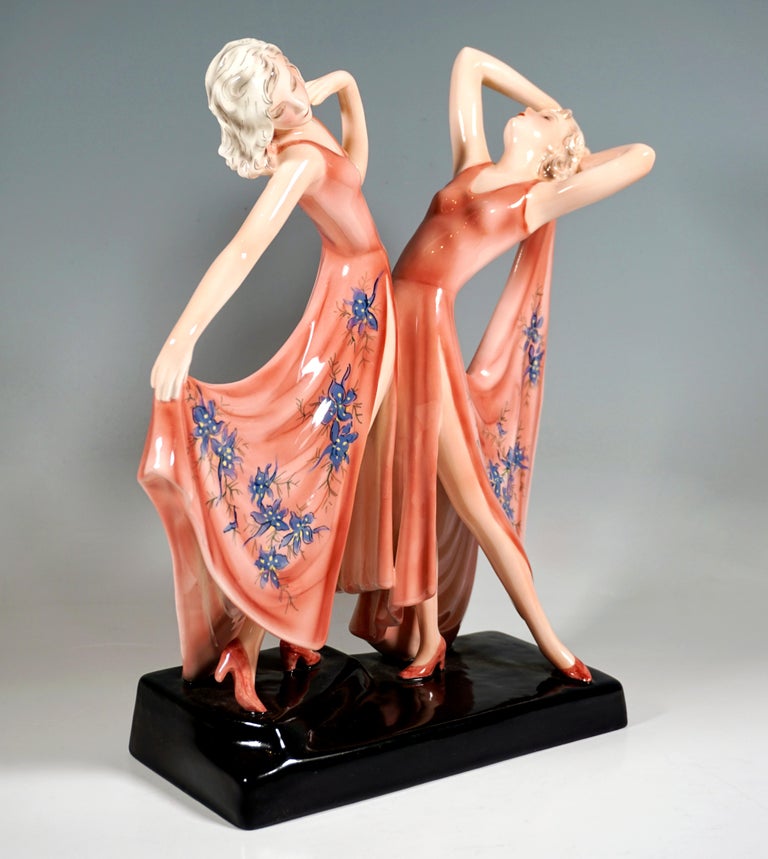 Rare Viennese Ceramic Art from the 1930s:
Two graceful dancers in long, deeply cut and high slit rose colored dresses with blue floral decorations, facing each other with their upper bodies leaning back and holding the skirt ends performing a dance