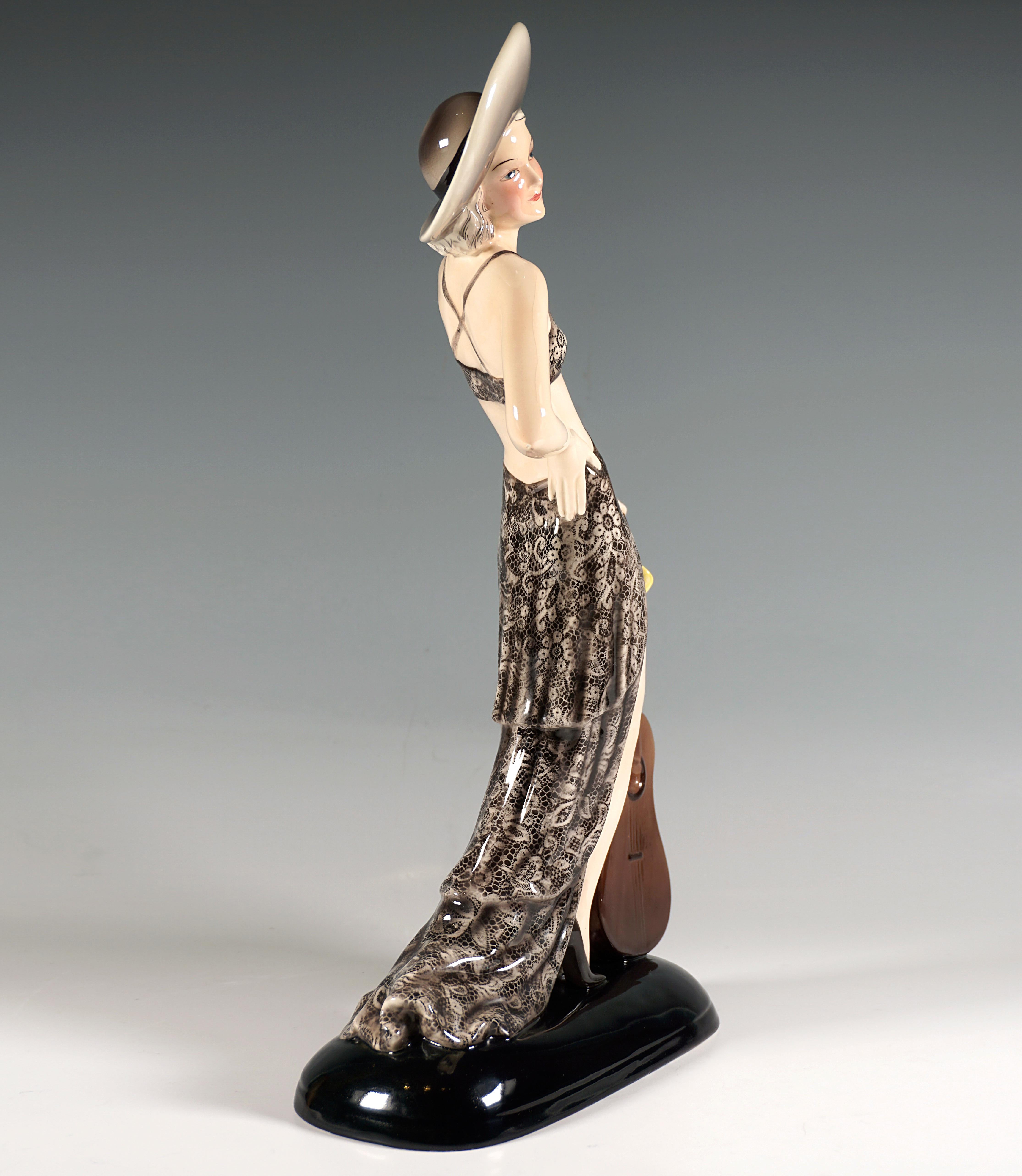 Rare and exclusive Goldscheider Art Déco Ceramic Figurine:
Posing young lady in a dark gray lace dress with a bustier attached to the front of the skirt, an elegant, wide-brimmed, light-colored hat on her blond curls, looking to the right and