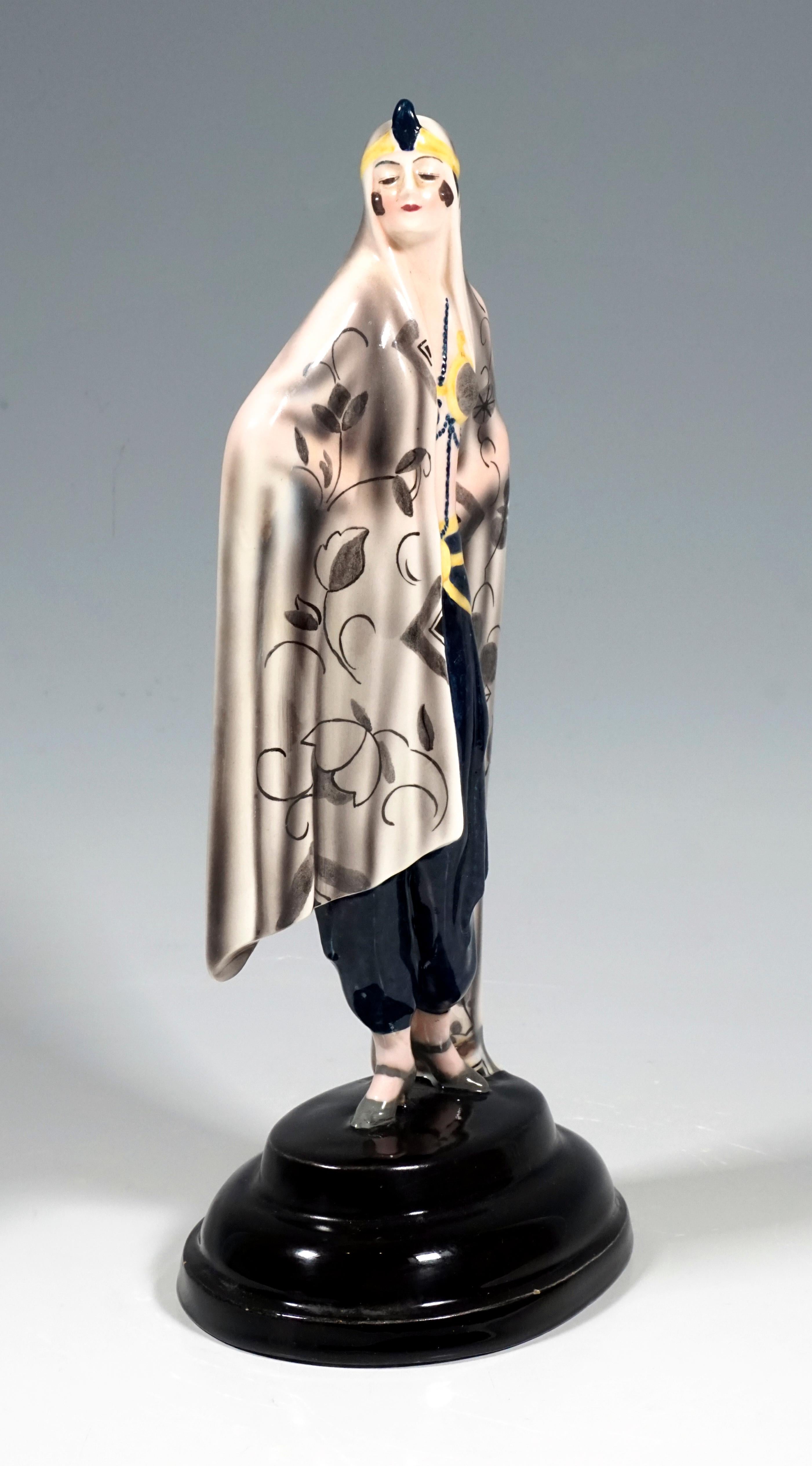 Darstellung einer stehenden, stolz zur Seite blickenden Dame in orientalischem Gewand. Sie ist in ein großes beigefarbenes Tuch gehüllt, das bis zum Boden reicht. Die Vorderseite ist mit einem stilisierten, grau schattierten Blumen- und Rankenmuster