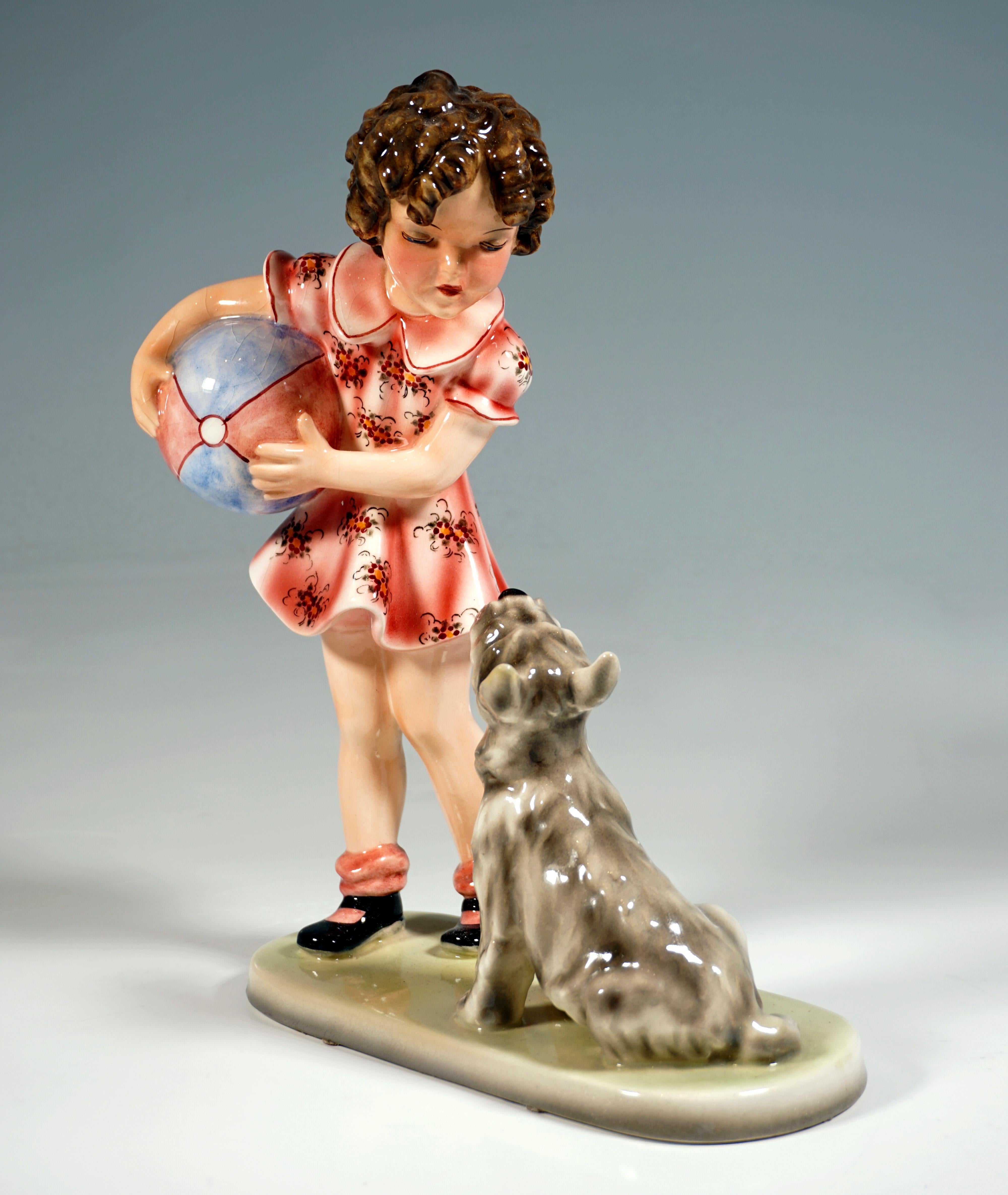 Kleines Mädchen mit lockigem Haar in einem geblümten Sommerkleid mit einem großen Ball unter dem Arm, der auf einen Terrier herabschaut, der neben ihr auf dem Boden sitzt, hechelt und auf ein Zeichen wartet.
Auf einem cremefarbenen, ovalen Sockel