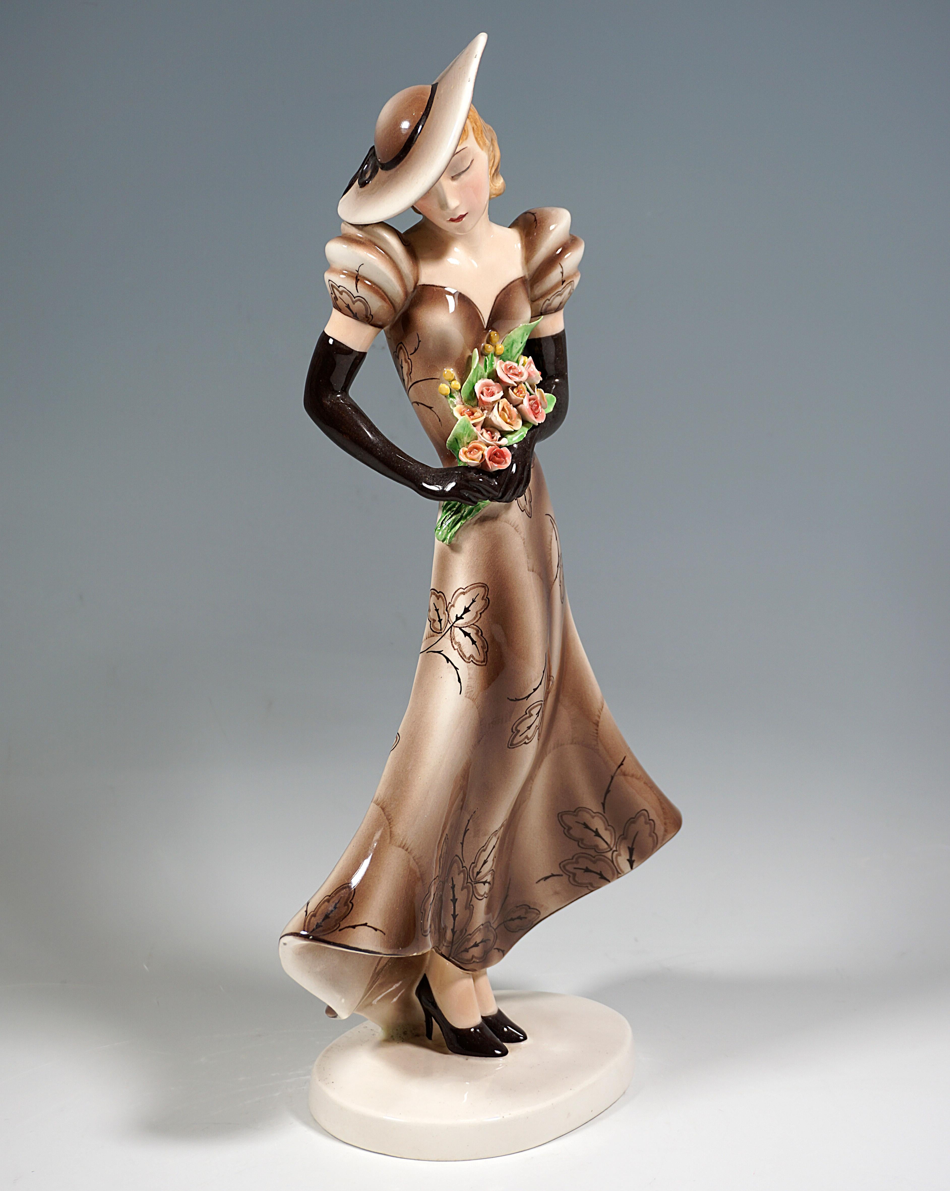 Rare Goldscheider Art Deco ceramic Figurine of the 1930s:
Elegant standing young blond lady in long light brown dress patterned with stylized leaves with low back, puffed sleeves and long gloves, her head with wide-brimmed brown hat tilted to one