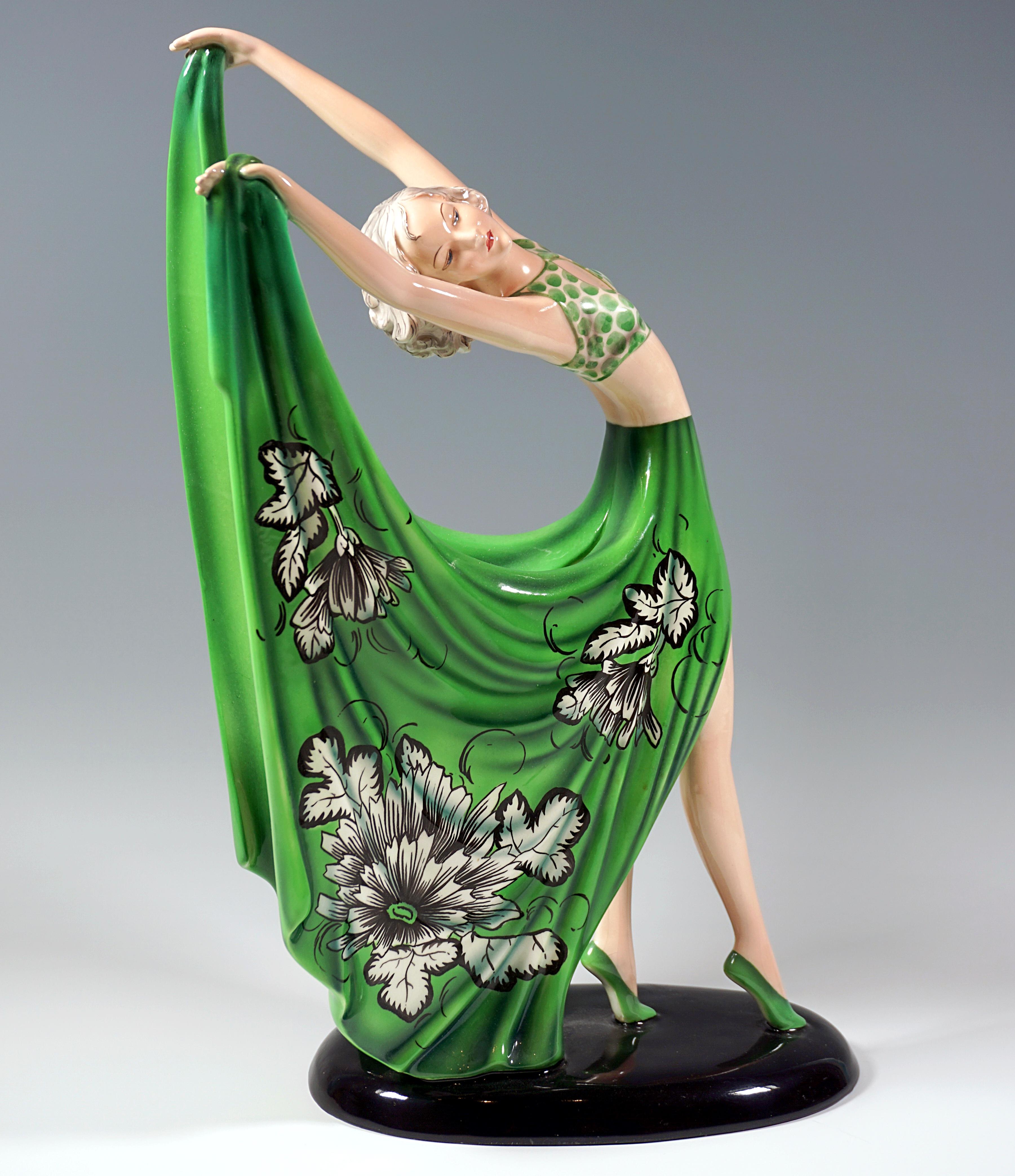 Delicate Goldscheider Art Déco Ceramic Figurine.
Gracefully posing dancer in a green costume: dotted bustier skirt short at the front with long, wide side parts that are slit on the back and decorated with white and black flowers, holding them up