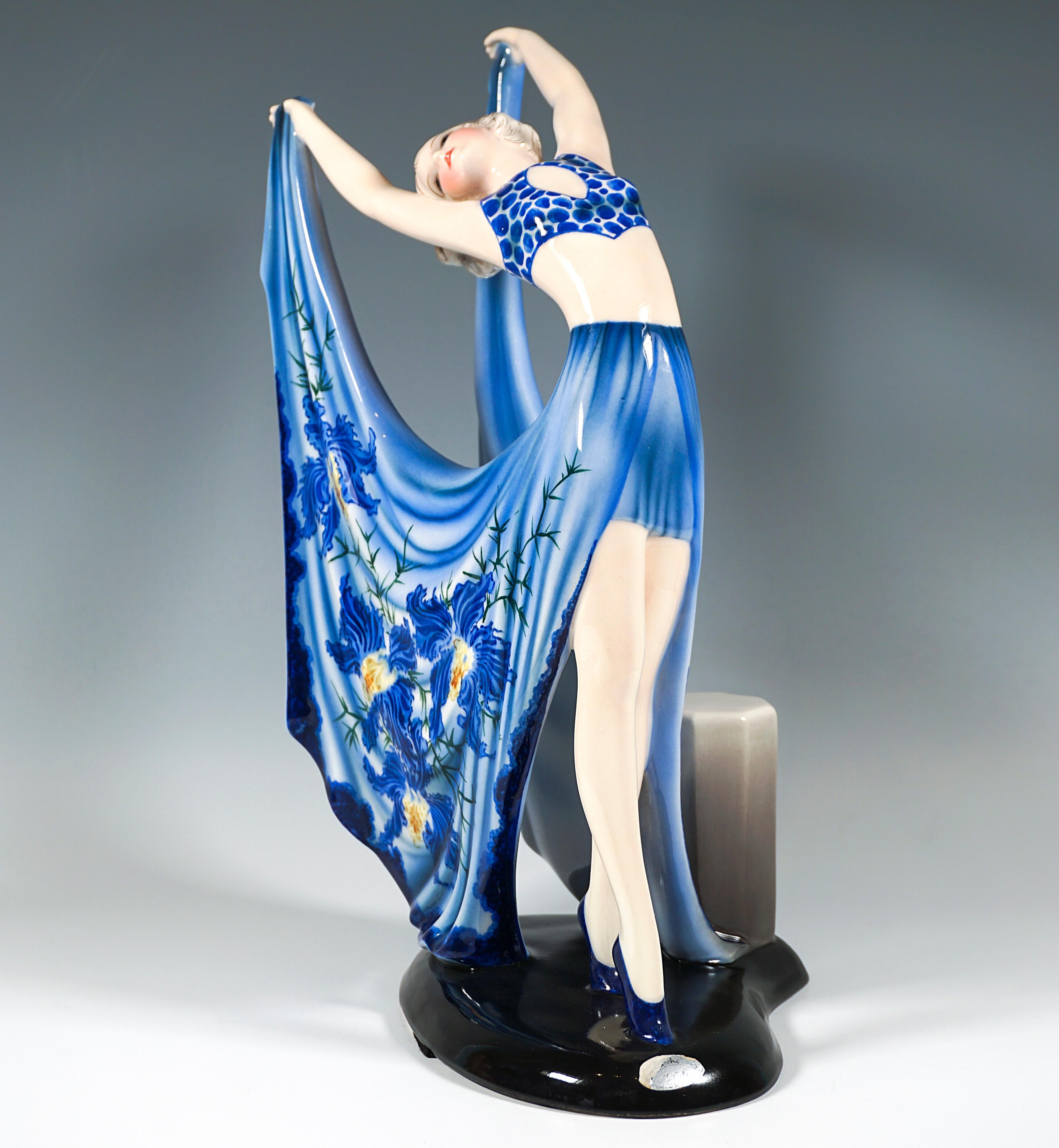 Zarte Goldscheider Art Déco-Keramikfigur aus den 1930er Jahren:
Anmutig posierende Tänzerin in blauem Kostüm neben einem achteckigen Podest stehend: gepunktetes Bustier und kurzer Vorderrock mit langen, weiten, hinten geschlitzten Seitenteilen mit