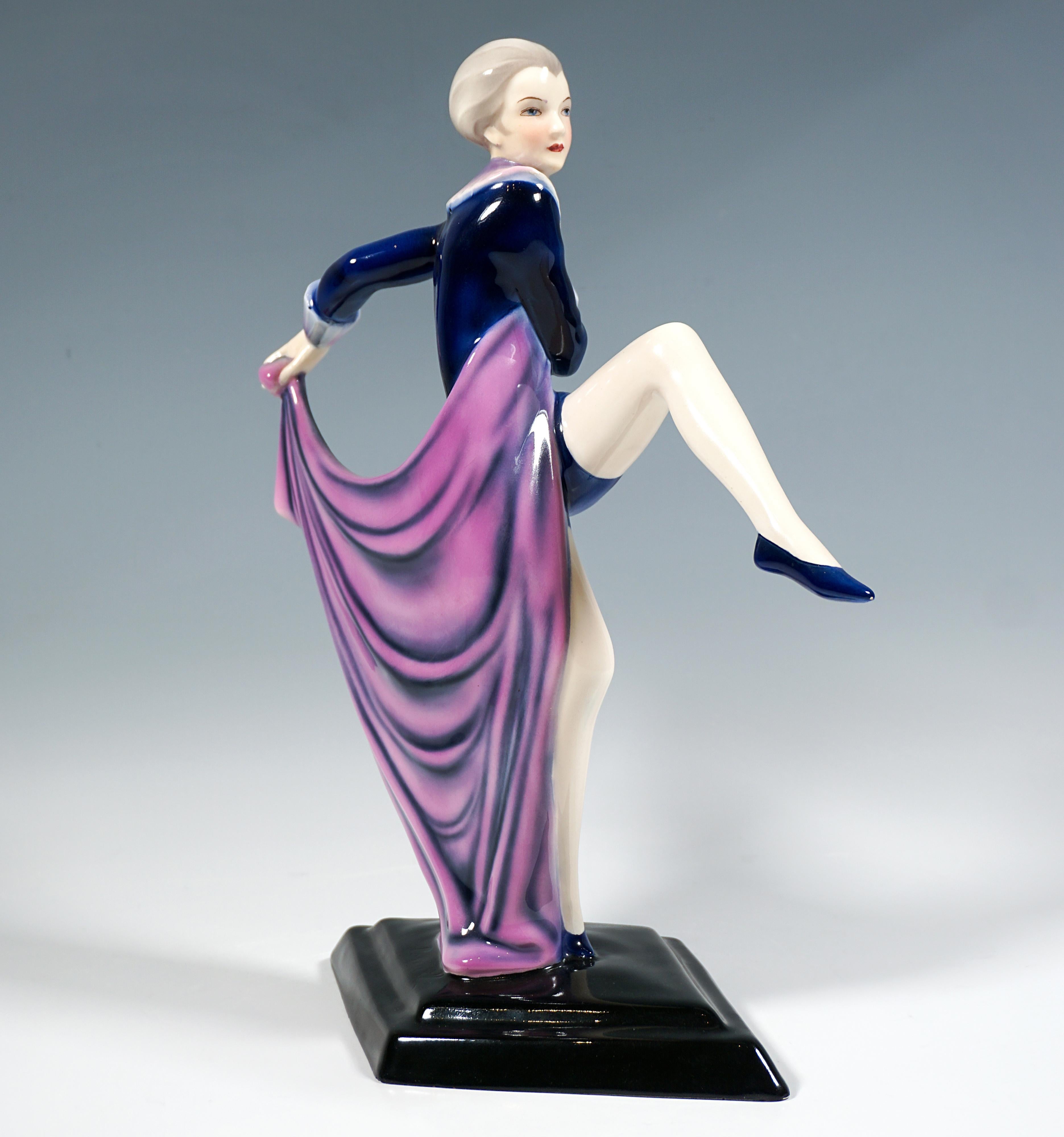 Exquisite ceramic figurine of the 1930:
Delicate dancer in a tight-fitting, dark blue costume with short legs and a pink and purple frill, on her feet gymnastic shoes, balancing on the ball of her right toe, throwing her left leg forward and up,