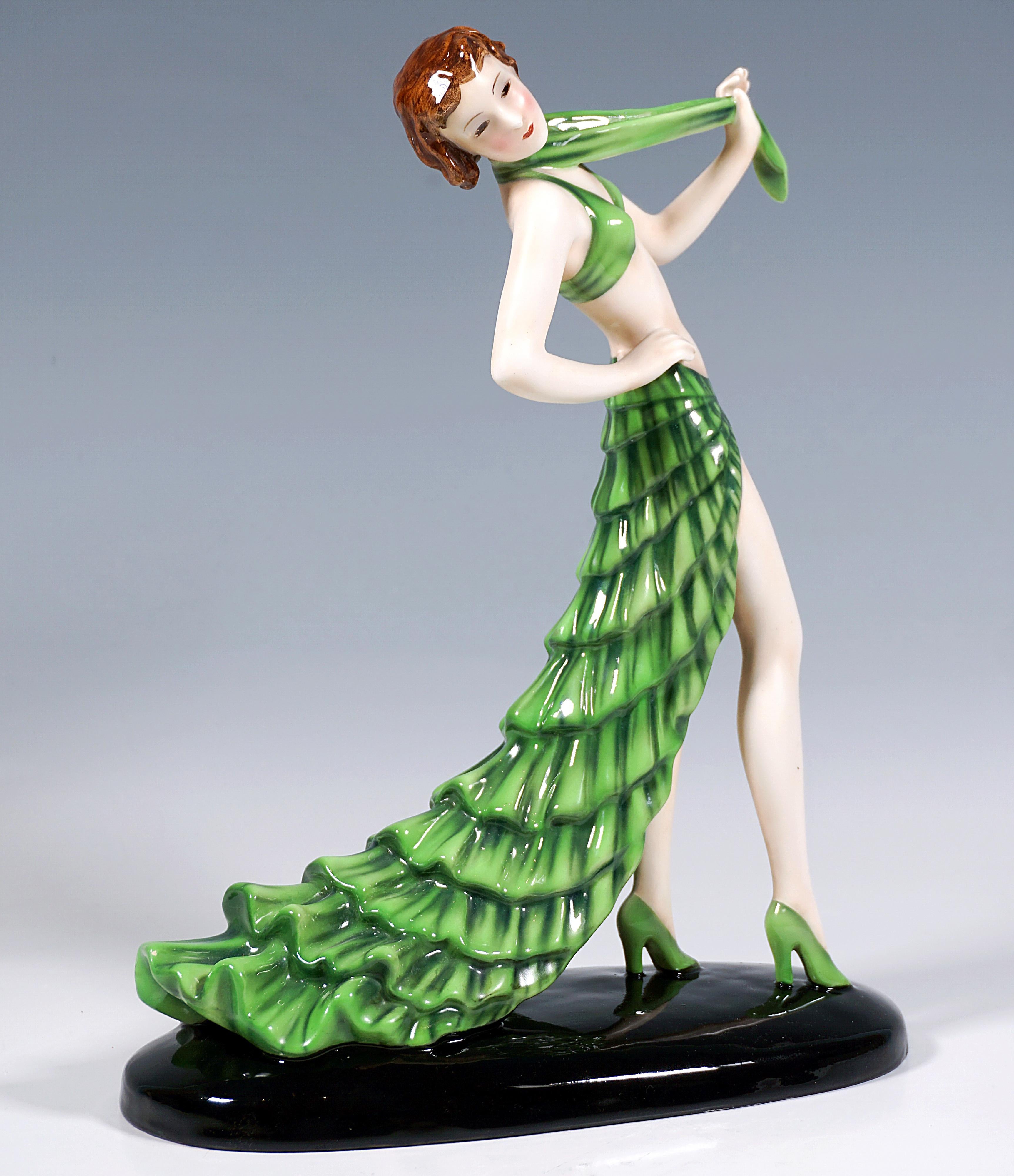 Délicate figurine en céramique Goldscheider Art Déco des années 1930 :
Jeune danseuse aux cheveux bruns courts, posant, vêtue d'un costume vert : un bustier moulant et une jupe courte et fendue à volants avec une longue traîne et des chaussures à
