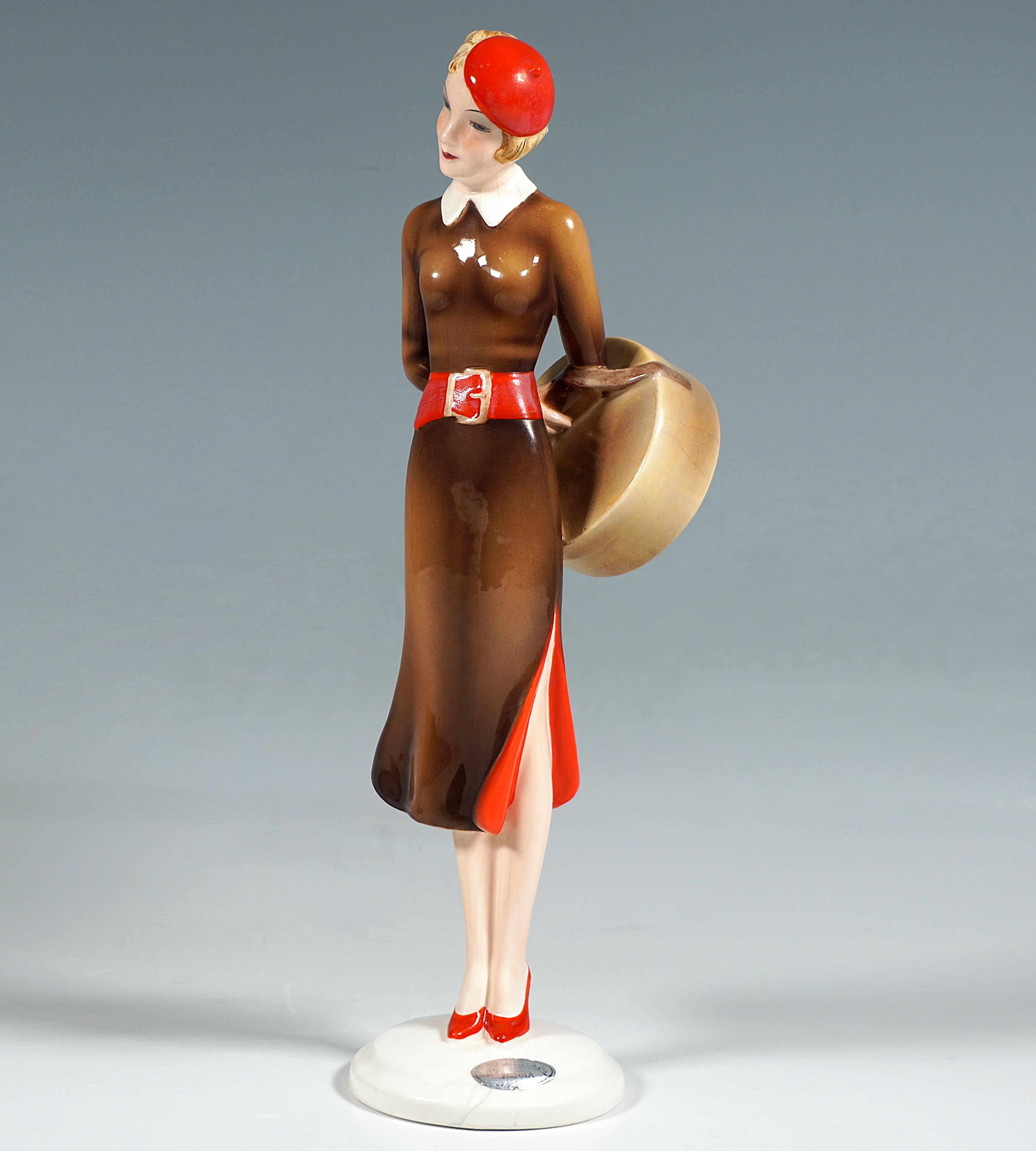 Very Rare And Excellent Goldscheider Ceramic Figurine of the 1930s:
Standing elegant young lady in brown dress with side slit, red lining and white collar, as well as red cap, wide red belt and red heeled shoes, arms crossed at the back, around the