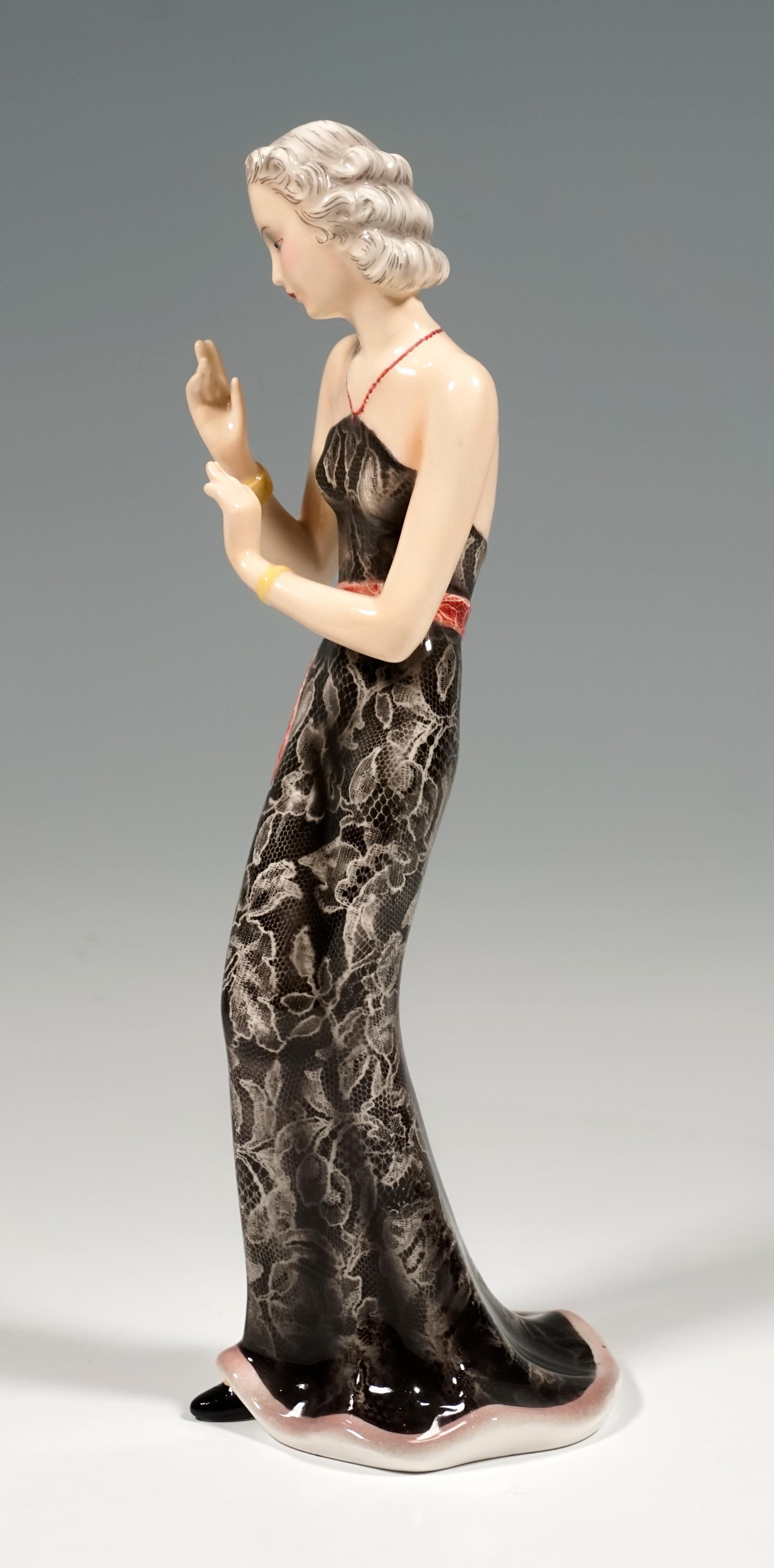 Représentation d'une dame élégante aux cheveux soigneusement épinglés, portant une longue robe moulante en dentelle noire sans bretelles, décolletée dans le dos, avec une longue ceinture rouge, tenant ses bras devant elle dans un geste élégant. On