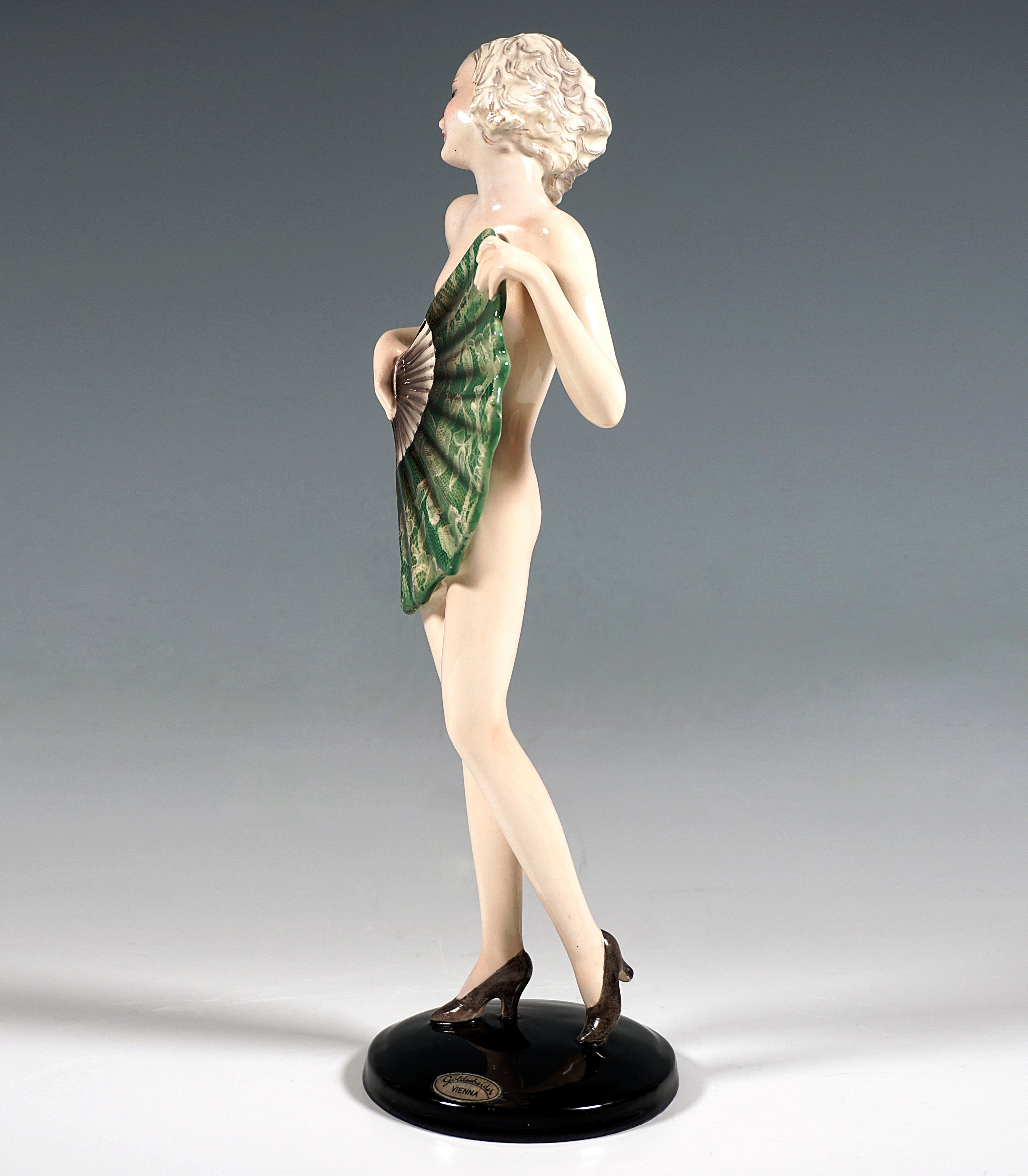 Rare And Excellent Goldscheider Ceramic Figurine of the 1930s:
Standing young lady with shoulder-length blond hair, dressed only in grey heels, looking over her shoulder to the left and holding a large fan covered with green lace in front of her
