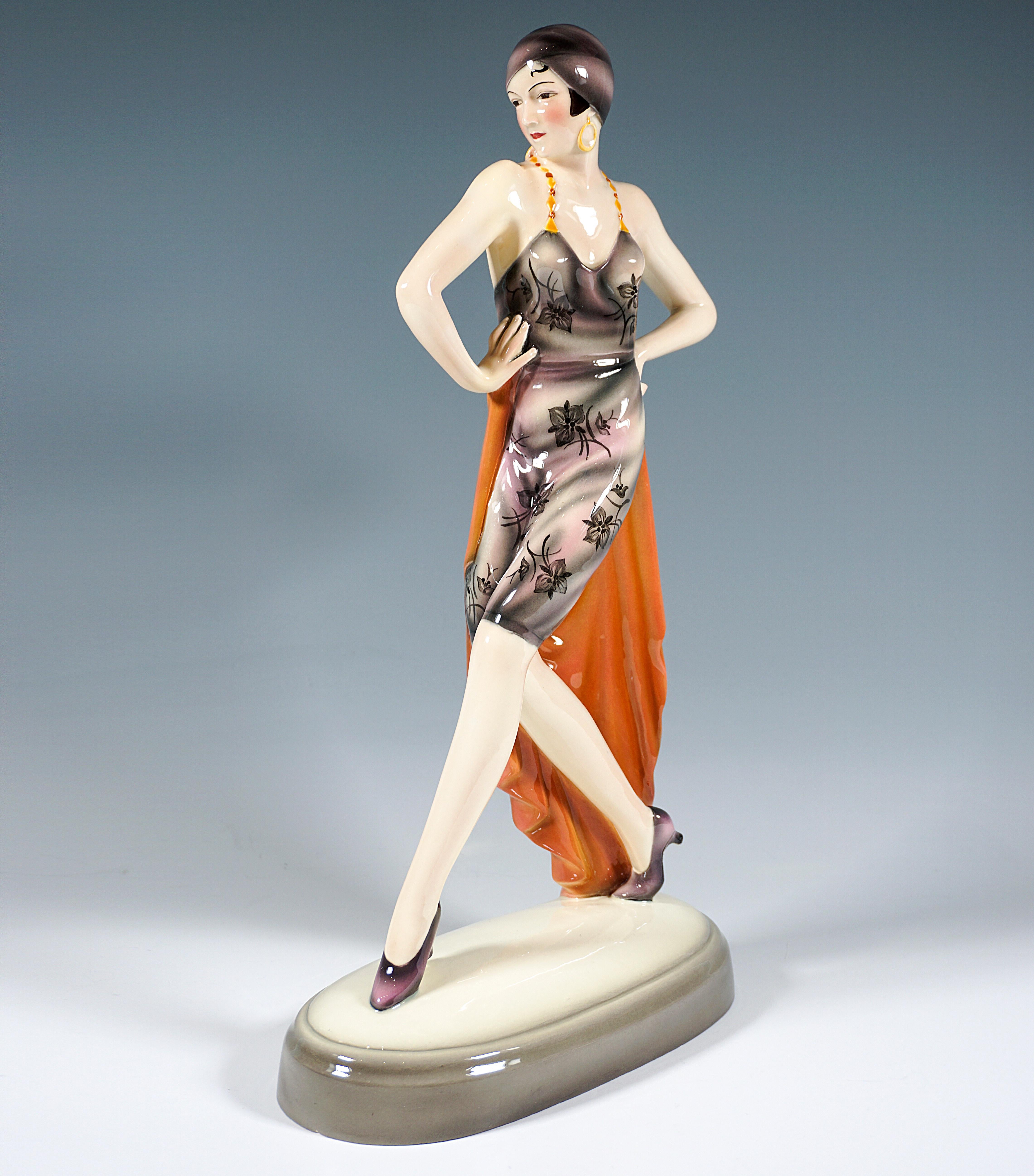 Extremeley rare porcelain figurine around 1930:
Elegant dancer striding to the side with her upper body turned forward, wearing a knee-length, shimmering gray-pink trouser dress with floral decoration, yellow-red pearl strap and low-cut back, and a