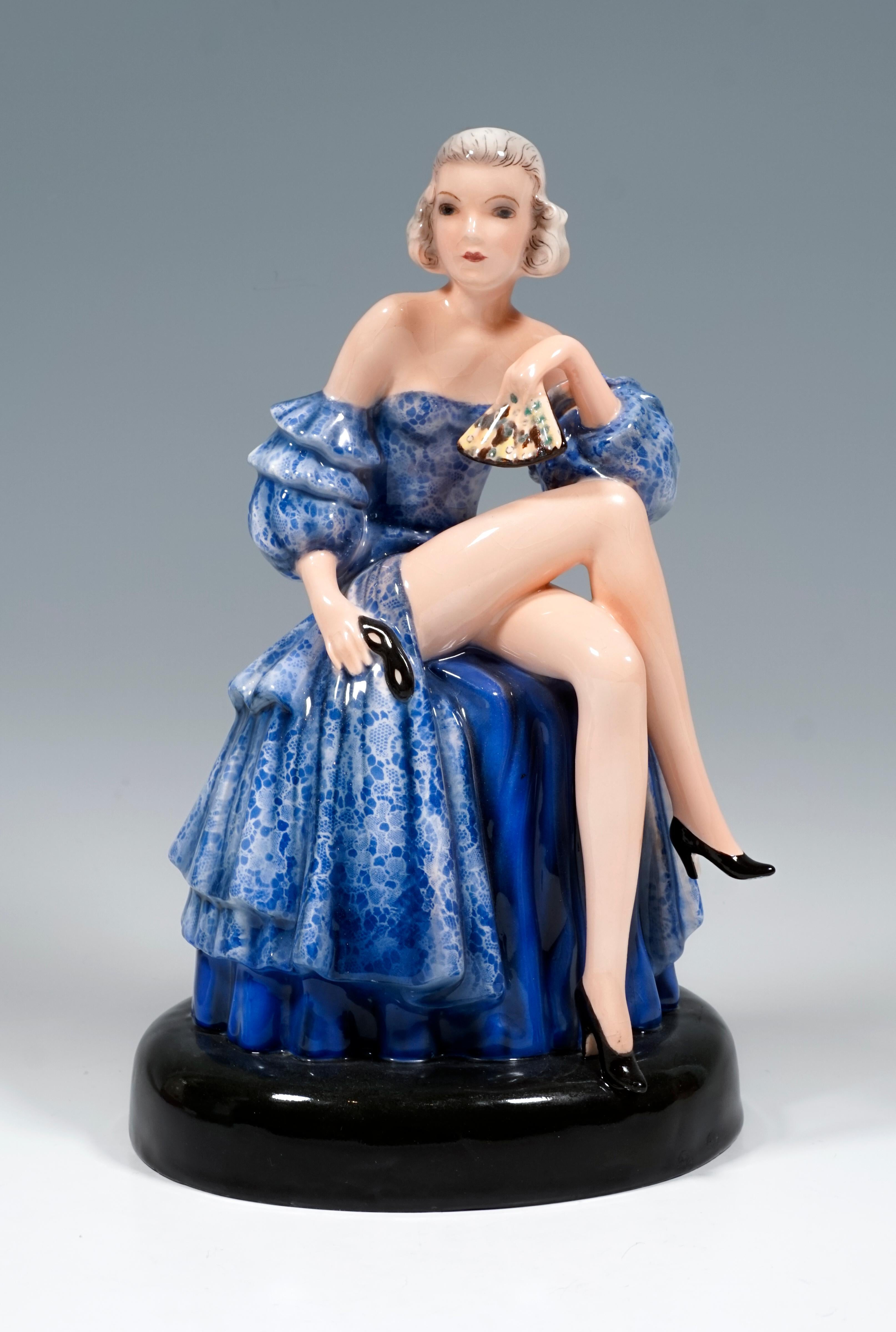 Rare Goldscheider Art Deco ceramic figurine:
Depiction of a seated dancer in a blue, strapless ball gown with lace flounces, the right leg folded over the left and the left arm on the knee, holding a ball mask and a fan in her hands.
The figure is