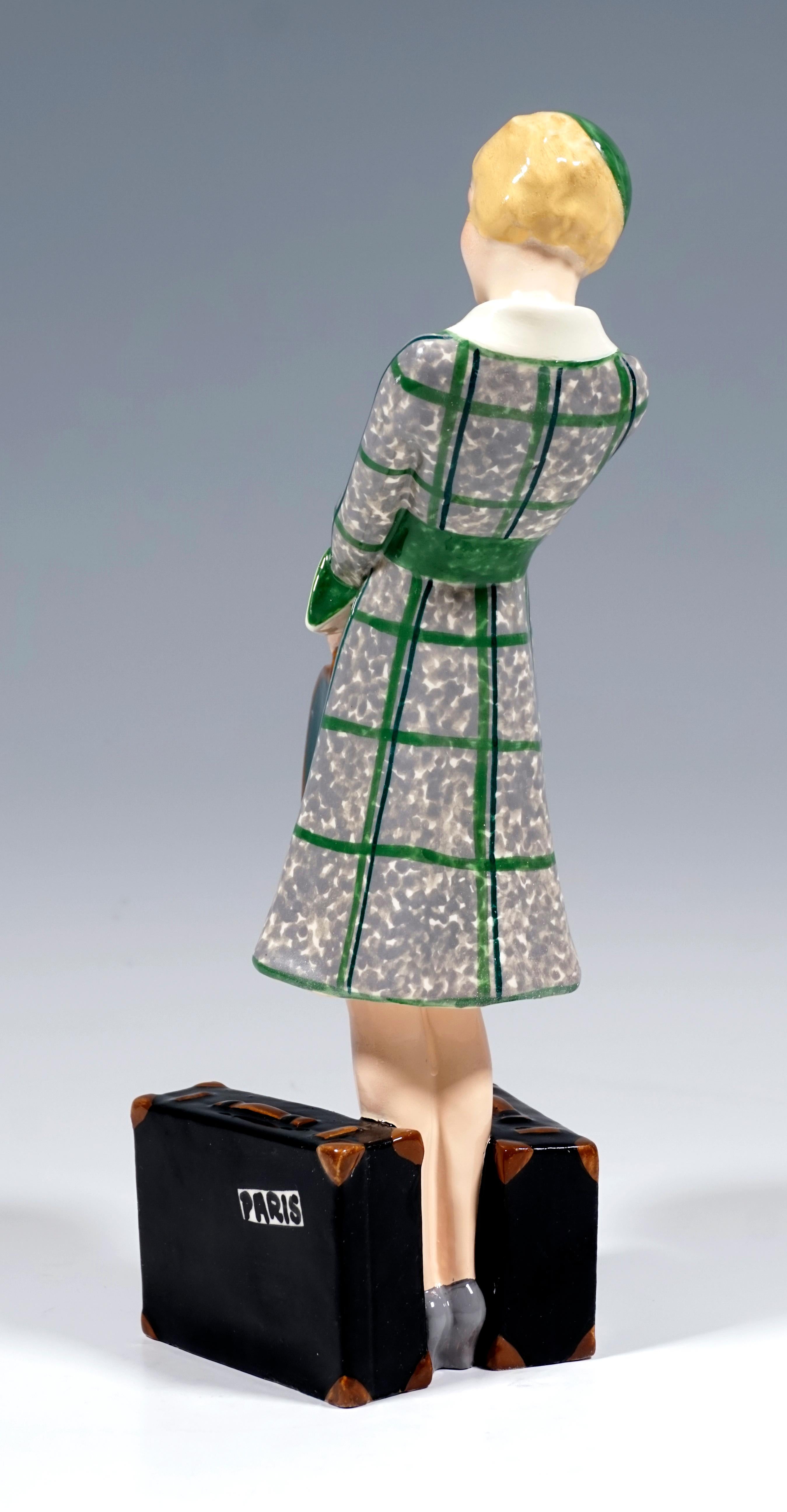 Very rare Goldscheider Vienna ceramic figurine of the 1930s:
Depiction of a blond, elegant lady in a gray-green dress and a matching hat standing between two black suitcases, holding a green bandbox in front of her with both hands.
The figure is