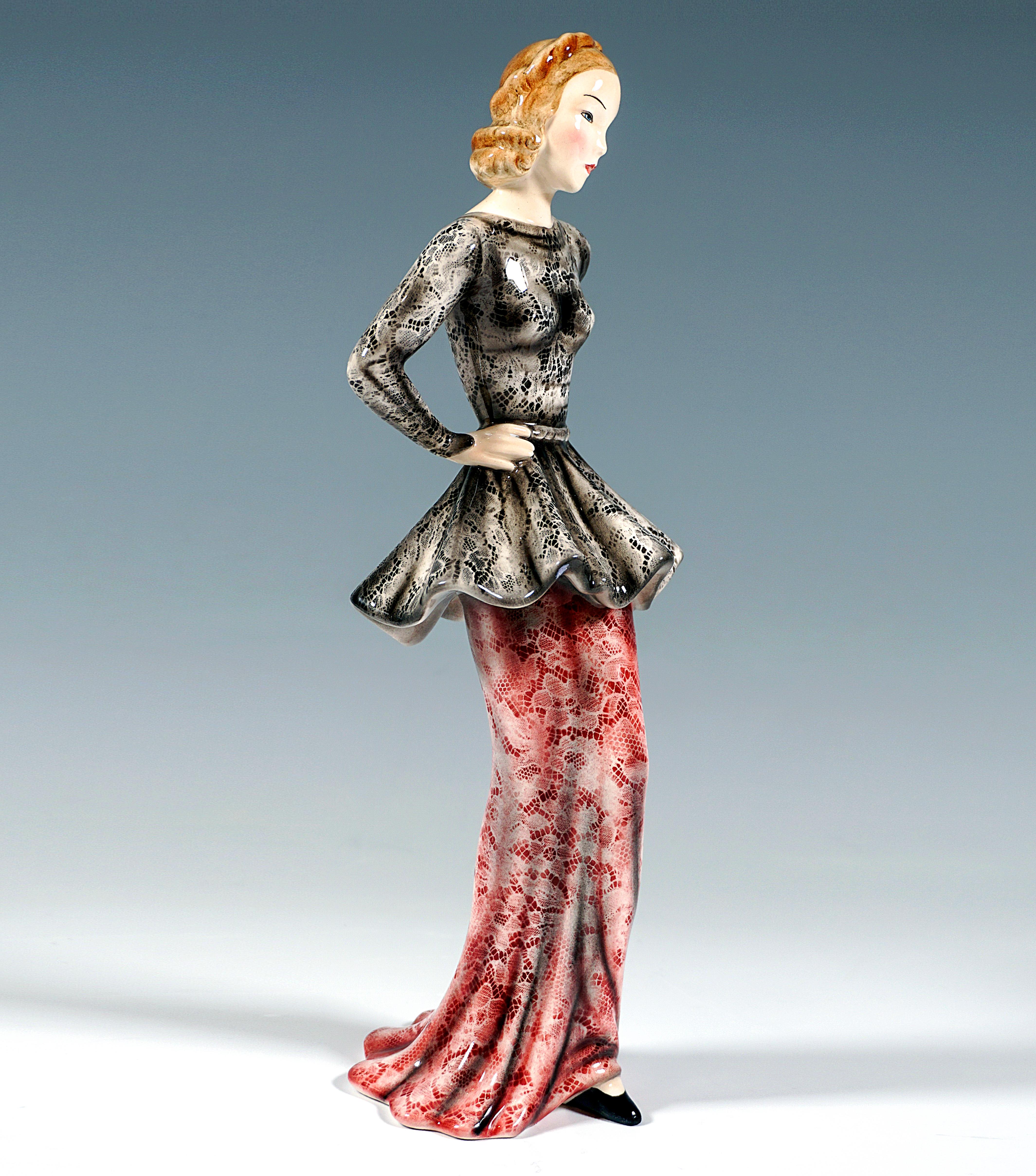 Darstellung einer eleganten, modischen Dame in langem, engem Spitzenrock in Rot mit schwarzem und weißem, hinten tief ausgeschnittenem, tailliertem Oberteil, die Arme auf die Hüften gestützt, ihr spitzer schwarzer Schuh ragt vorne unter dem Gewand