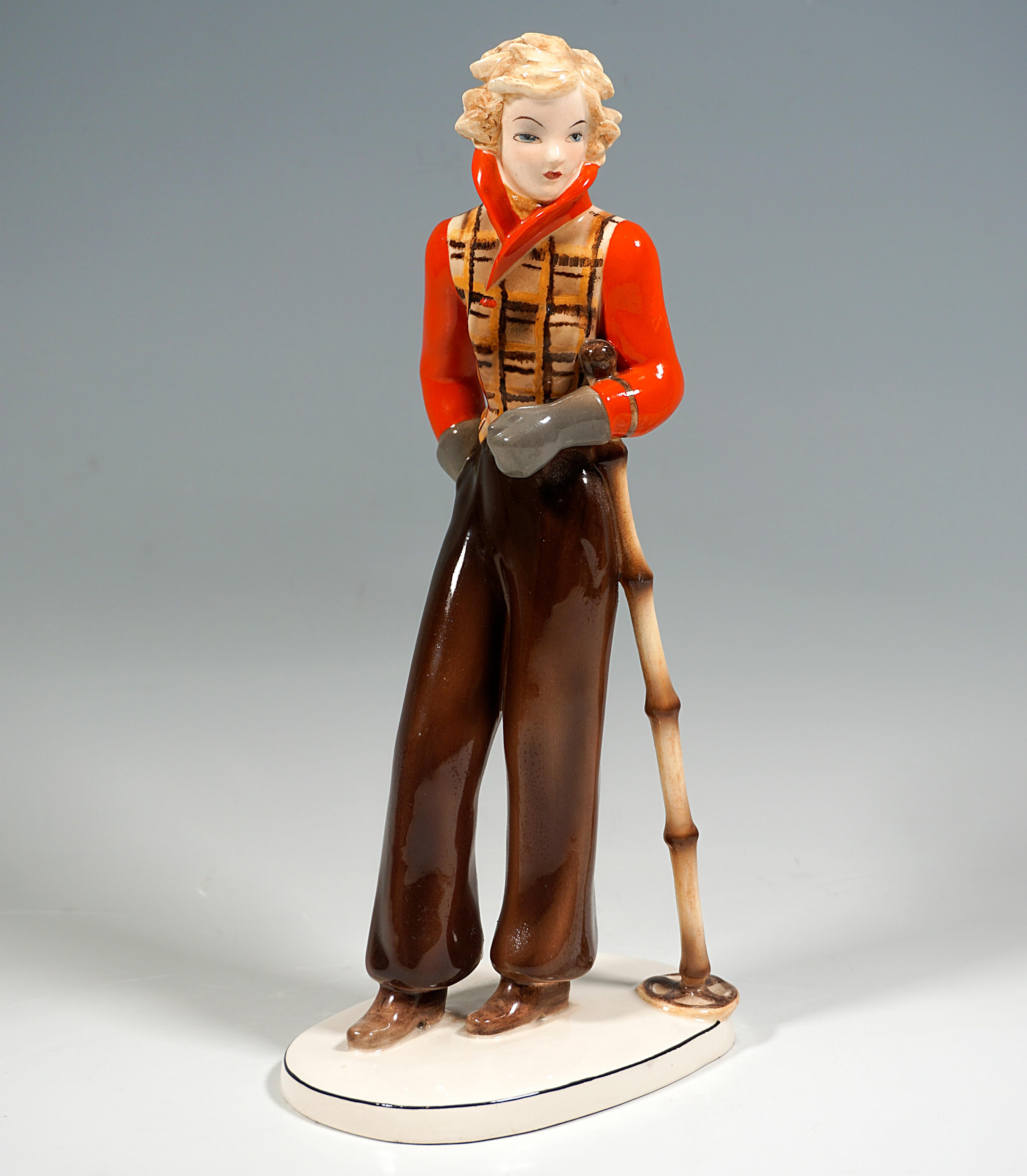 Goldscheider Art Ceramic Figure from the 1930s:
Young lady with blond curls dressed in ski fashion common in the 1930s: top checked in brown-orange tones with plain bright red sleeves and collar, dark brown wide ski pants and gray mittens, standing