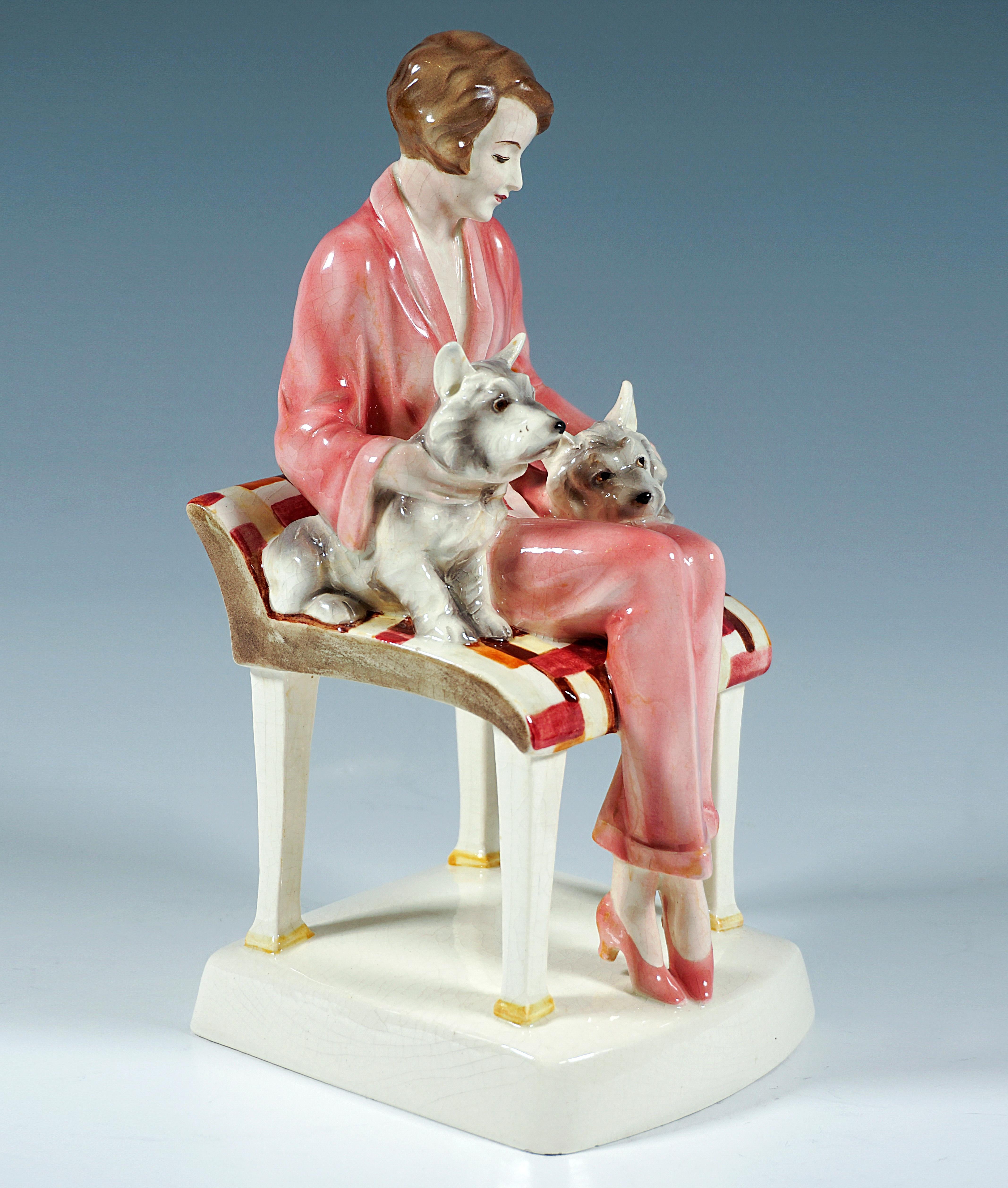 Excellent Goldscheider Figure Group of the 1930s:
Young lady in rosé pantsuit with brunette short haircut sitting on a large stool with low back support, embracing with both hands two terrier dogs that nestle on her left and right leg and lovingly