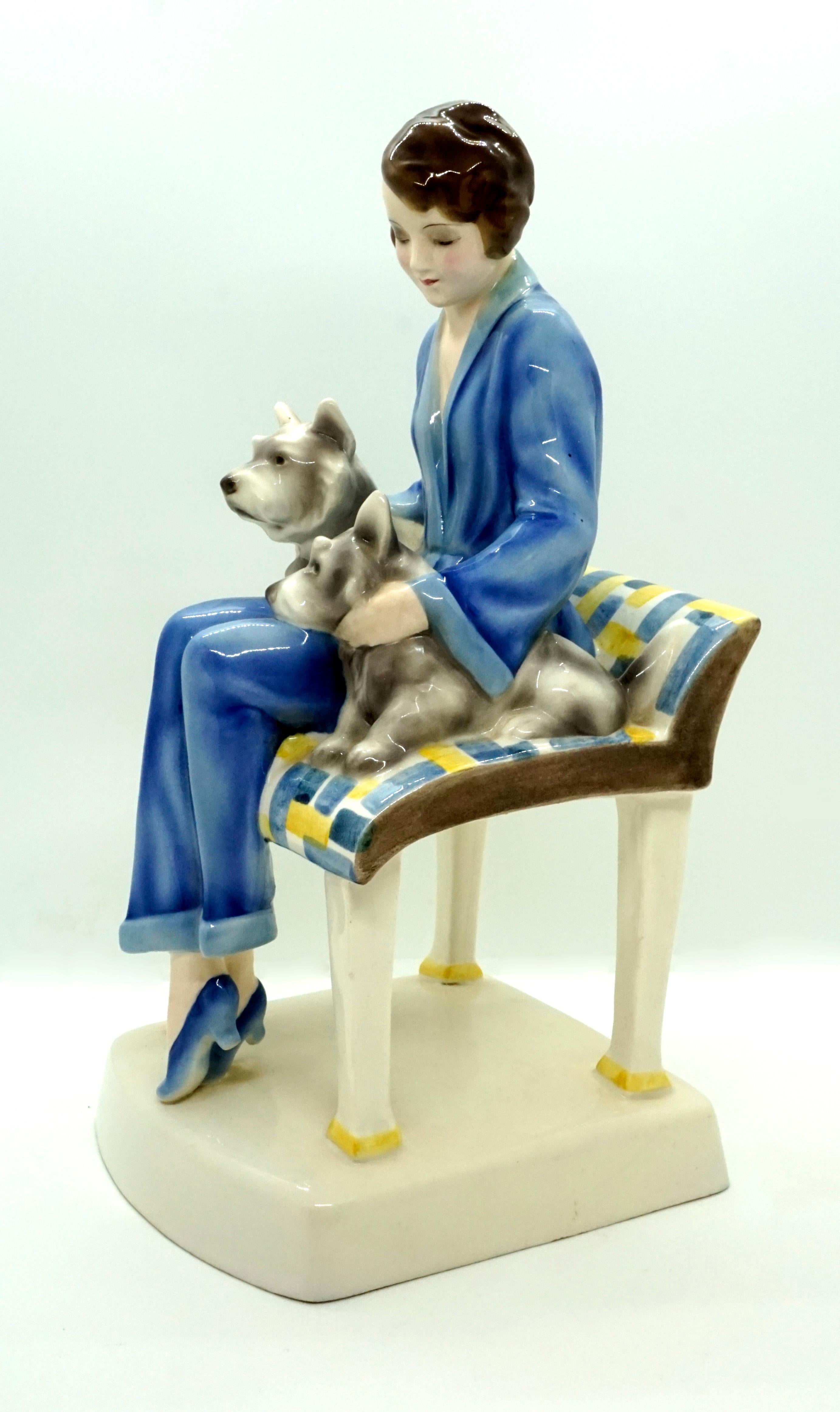 Rarest Goldscheider Figure Group of the 1930s.
The young lady in a blue trouser suit with a short brunette hairstyle sits on a large stool with a low backrest. With both hands, she hugs two dogs that nestle against her legs on the left and right.