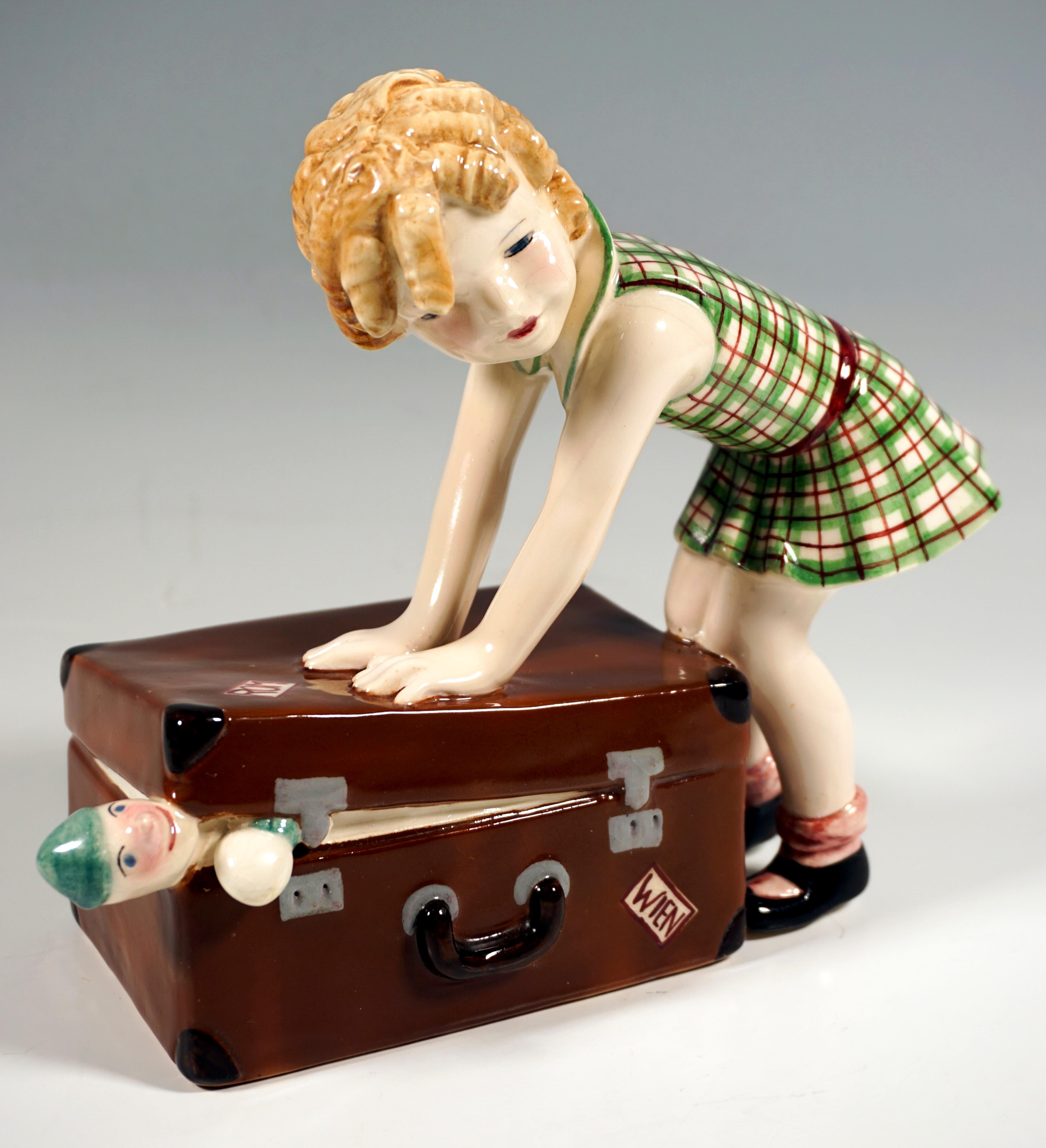 Rarísima figurita de cerámica Art Déco goldscheider de los años 30:
Niña rubia de pelo rizado con un vestido a cuadros verde-rojo, agachándose con ambas manos y utilizando el peso de su cuerpo para empujar una gran maleta marrón y cerrarla, lo que