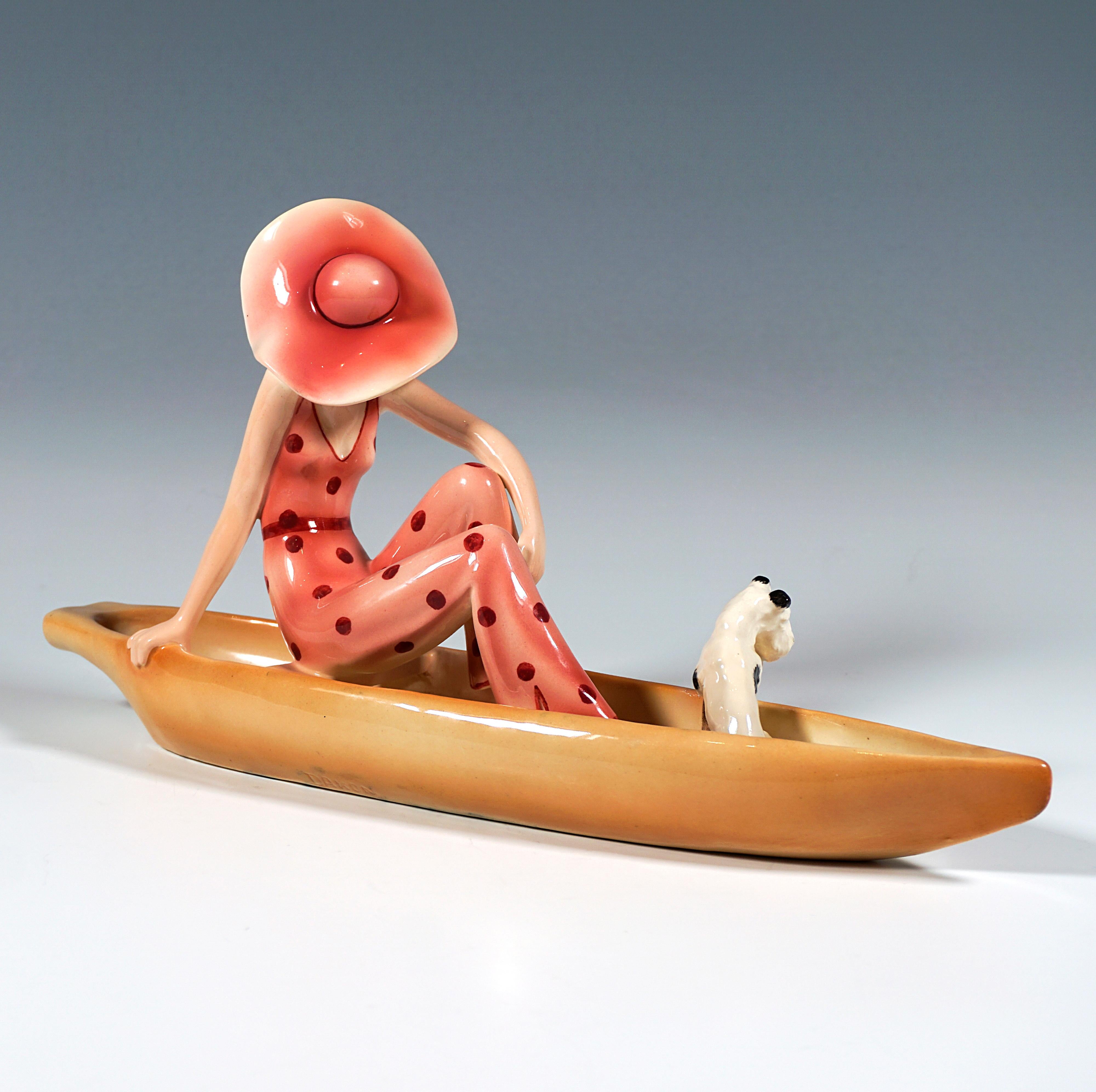 Rare et délicate figurine en céramique Goldscheider Art Déco des années 1930 :
Élégante jeune femme en costume pantalon rouge à pois rouges et grand chapeau sur ses cheveux blonds bouclés posant dans un bateau, à ses pieds un fox-terrier pied blanc