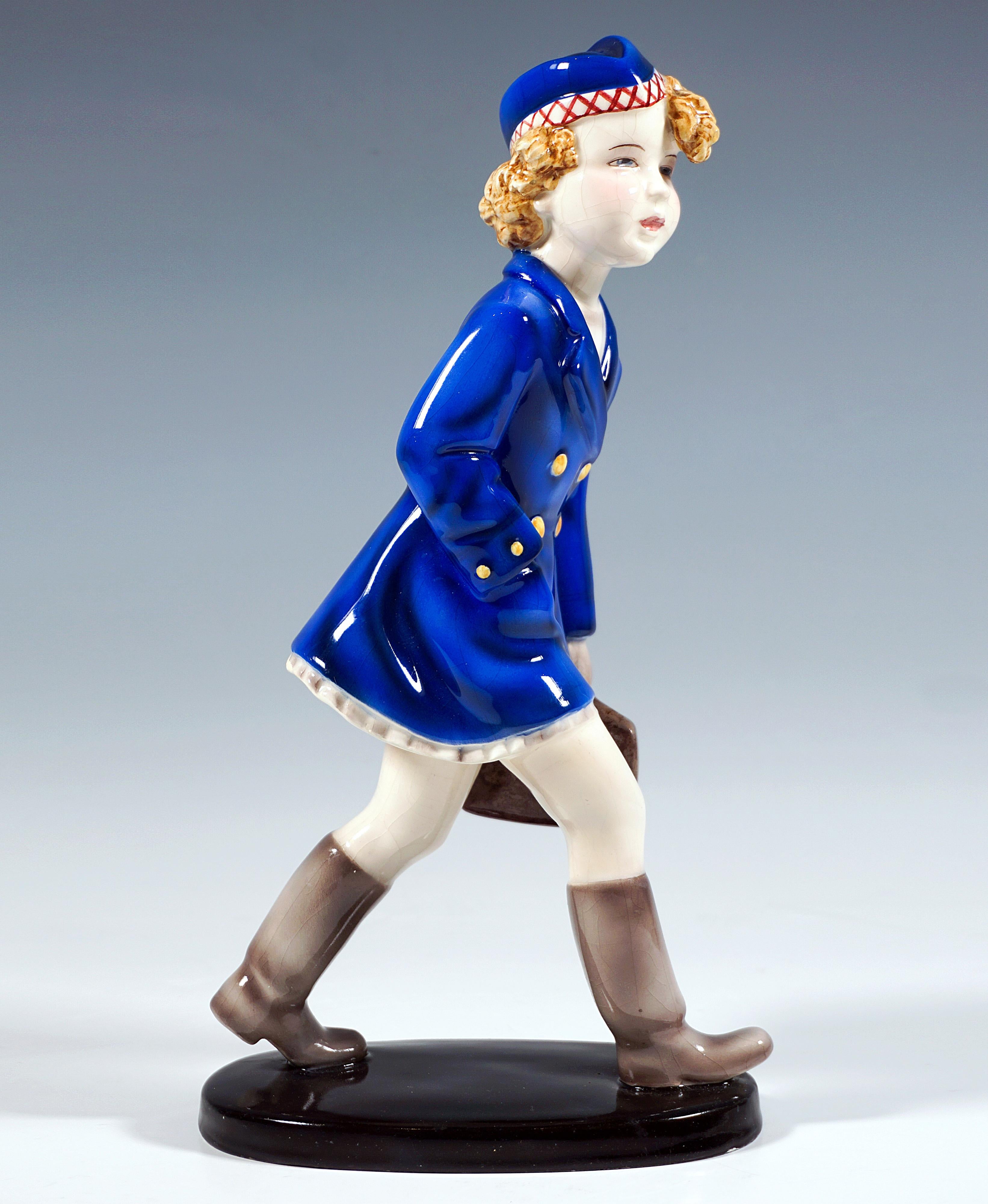 Rarísima Y Excepcional Figura De Cerámica Art Déco Goldscheider:
Niña a grandes zancadas con abrigo azul sobre vestido beige y gorro azul a juego con borde beige con bordado rojo, botas y guantes grises, la mano derecha enterrada en el bolsillo del