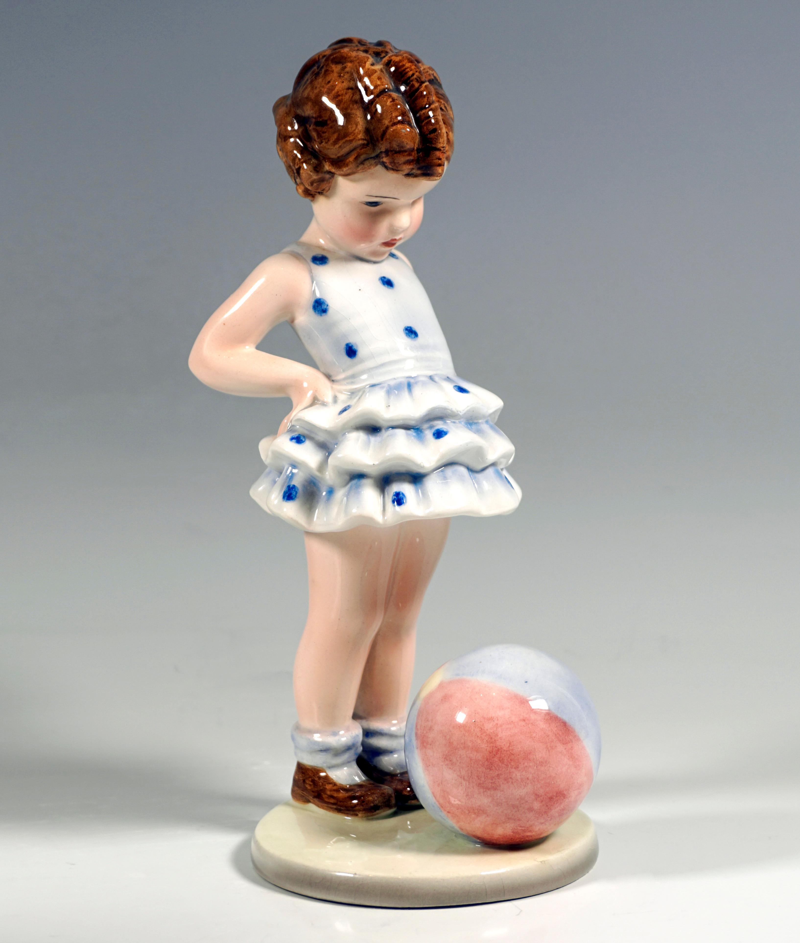 Petite fille bouclée dans une robe bleue à pois, les mains sur les hanches et regardant un ballon devant elle.
Sur une base ronde et plate de couleur beige.

Designer :
GERMAINE BOURET (1907 - 1953)
Dessinateur, caricaturiste, s'est fait