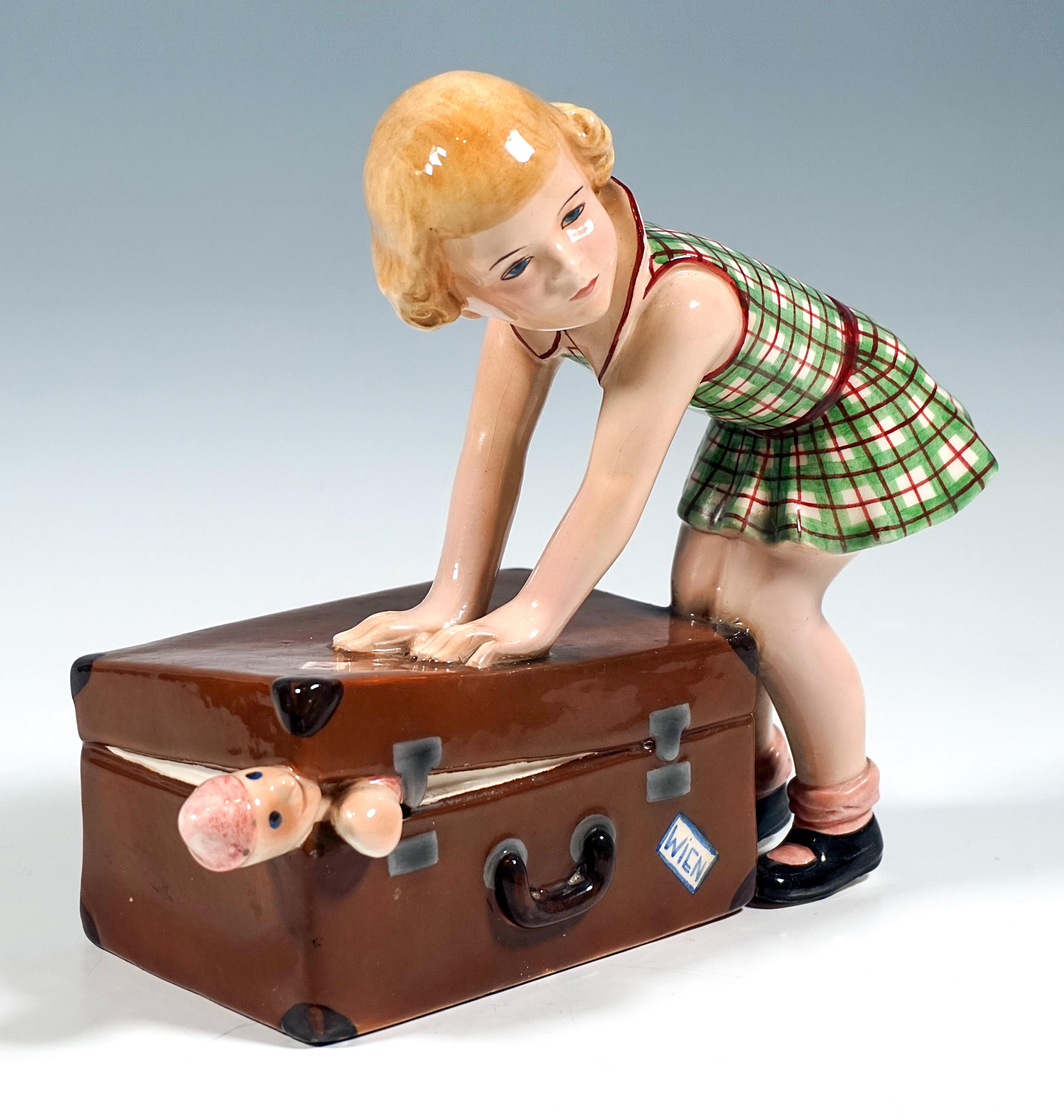 Rarísima figura de cerámica Art Déco Goldscheider de los años 30:
Niña rubia de pelo rizado con un vestido a cuadros verdes y rojos, agachada, intentando con ambas manos y el peso de su cuerpo cerrar una gran maleta marrón, lo que no consigue debido