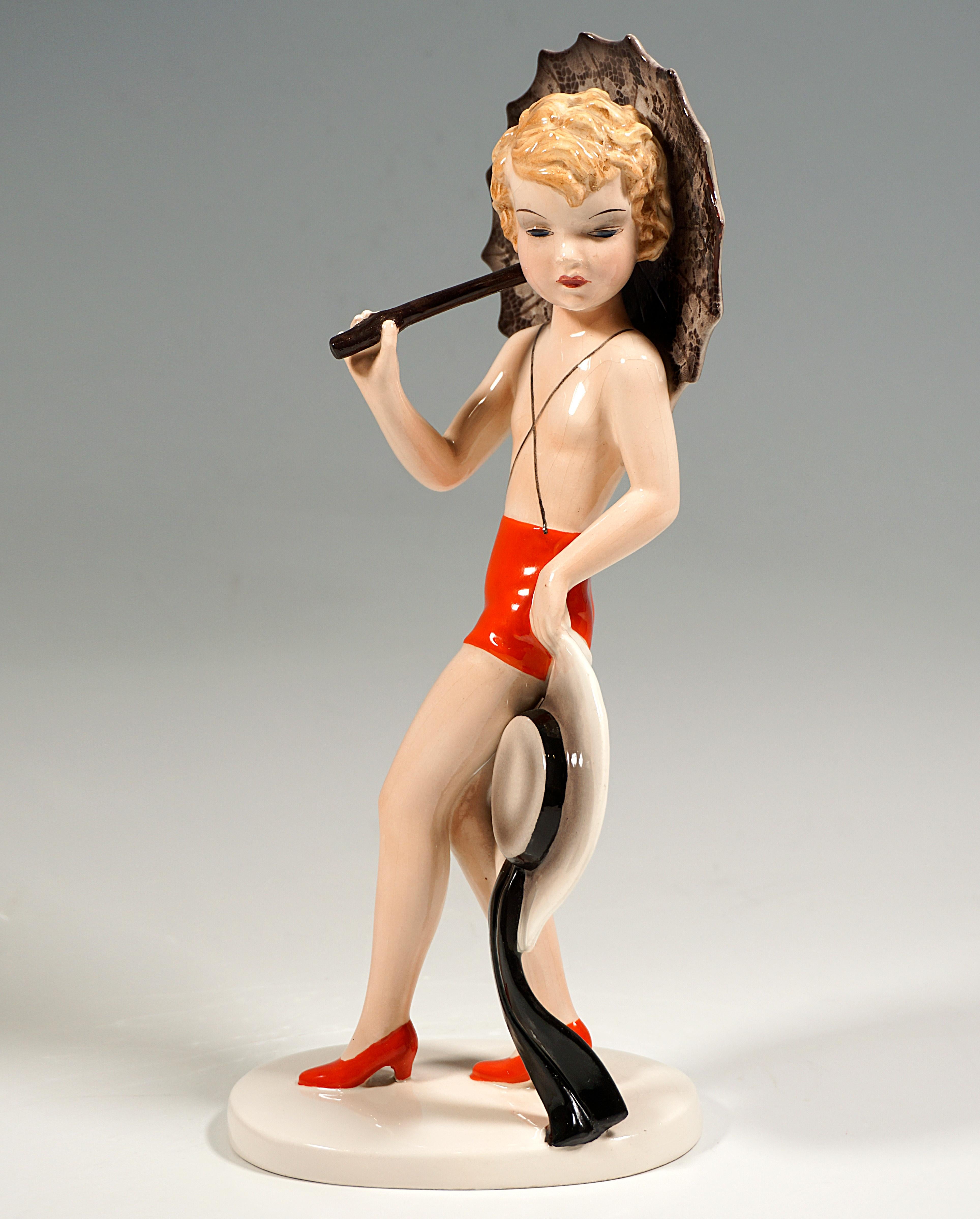 Extremely Rare Goldscheider Art Déco Ceramic Model Of The 1930s:
Blonde young girl, dressed only in red shorts with crossed suspenders and red heels, posing with a black lace umbrella and a large beige hat.
On an oval, cream-colored flat base,