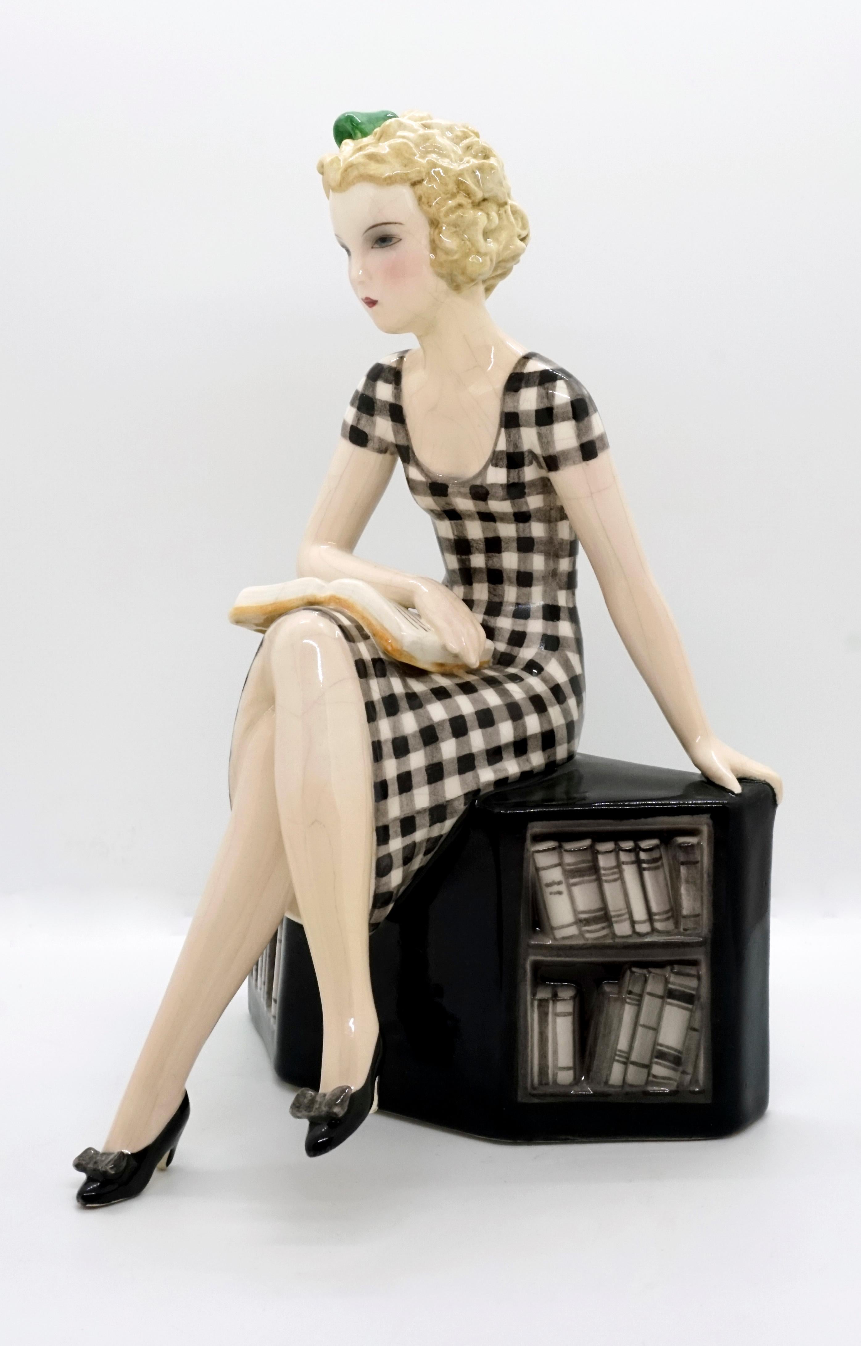 Very rare goldscheider Art Deco ceramic figurine.
The girl with blond curly hair and a green bow in her hair, wearing a black and white checked dress, is sitting cross-legged on a low black bookshelf. Looking lost in thought, she lays her right