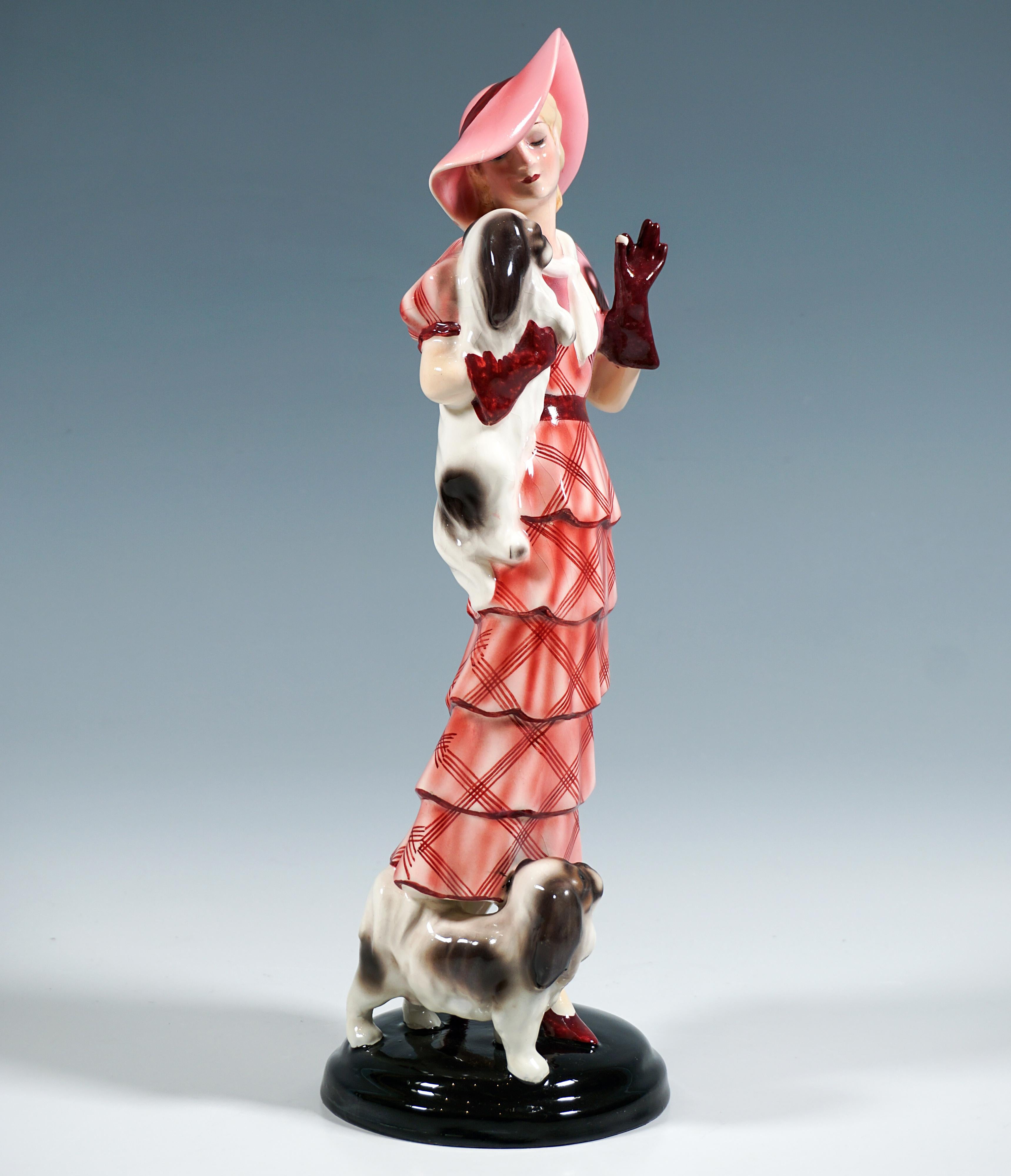 Rara y delicada figurita de cerámica vienesa Goldscheider de los años 30:
Representación de una elegante dama de pie, con vestido largo rojo de cuadros con volantes escalonados, sombrero a juego y guantes rojos, que sostiene a un pequinés en el