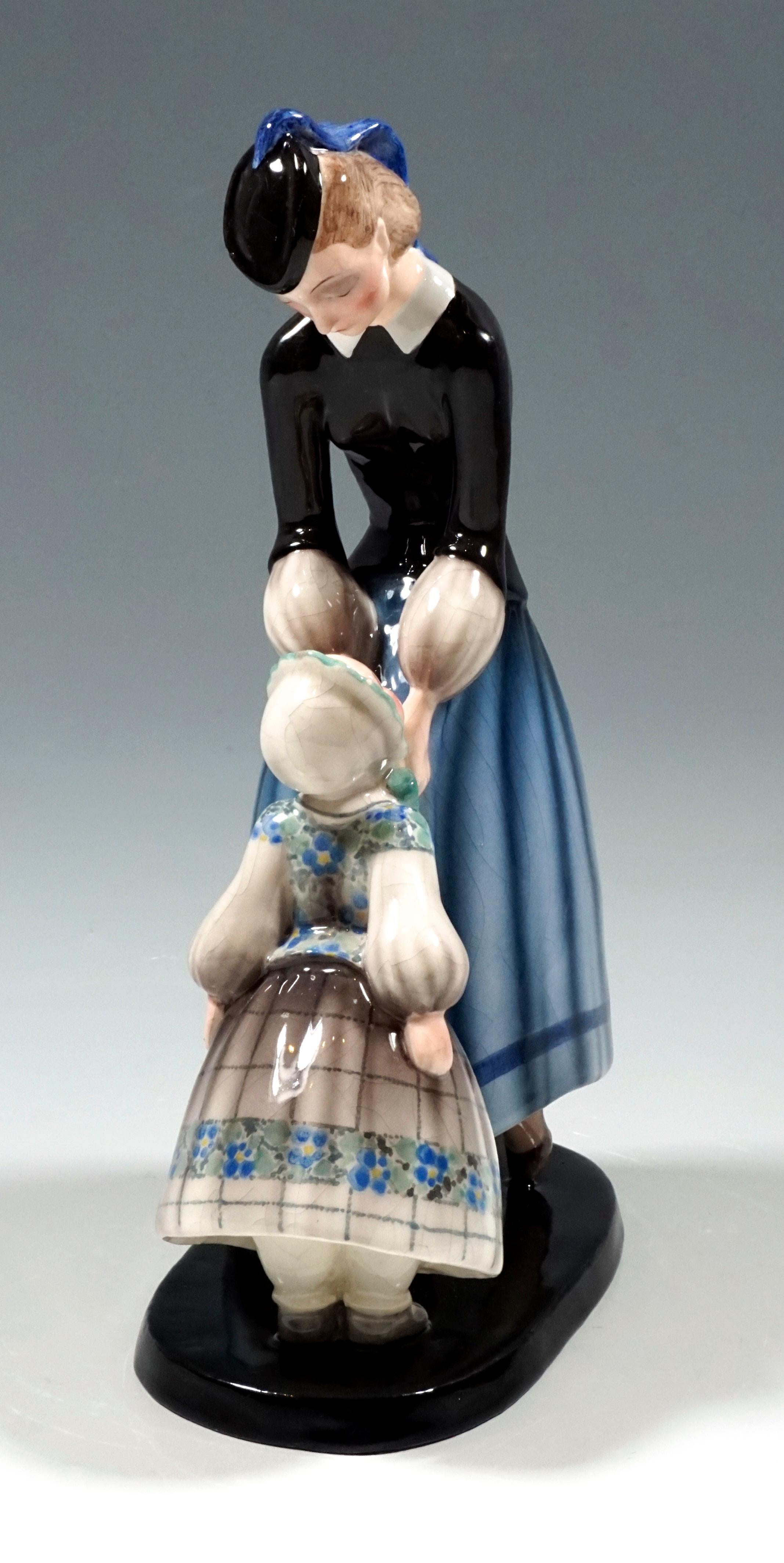 Especially rare Goldscheider ceramic figurine group
The woman wears a black cap with a blue bow that falls on her back, a black fitted jacket over a white blouse and a long, wide, blue skirt. She bends forward and reverently ties the bow around the